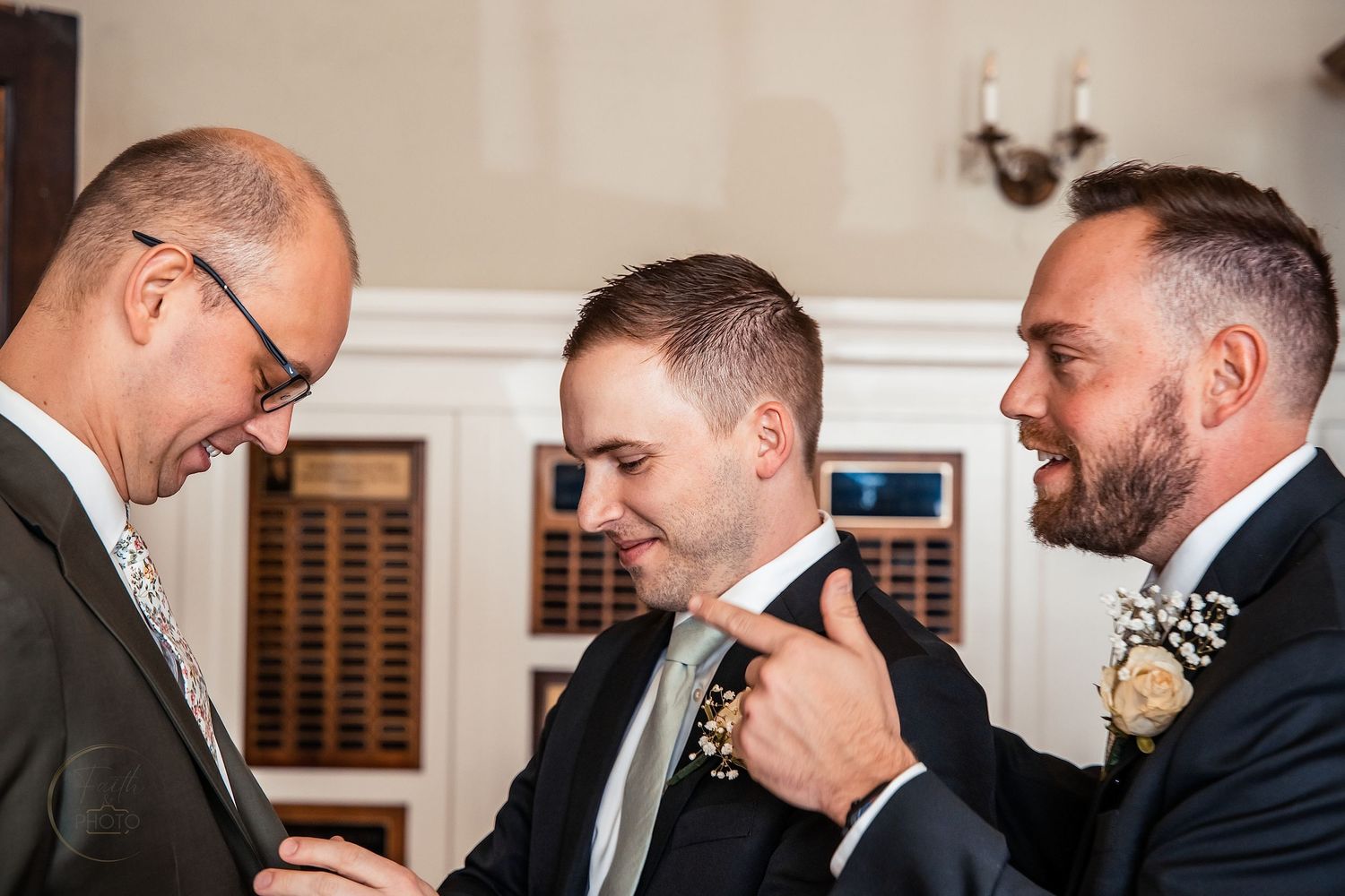 Two groomsmen help the groom adjust his boutonniere and tie before the wedding ceremony.