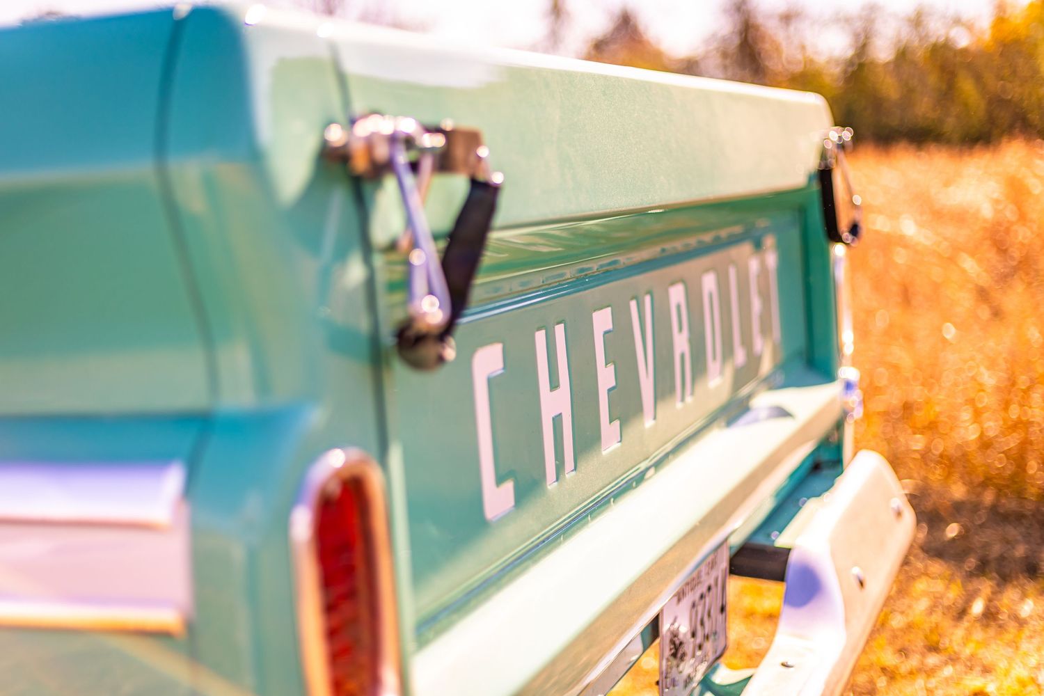 A vintage turquoise and white camper trailer parked in a scenic autumn setting with golden foliage in the background.
