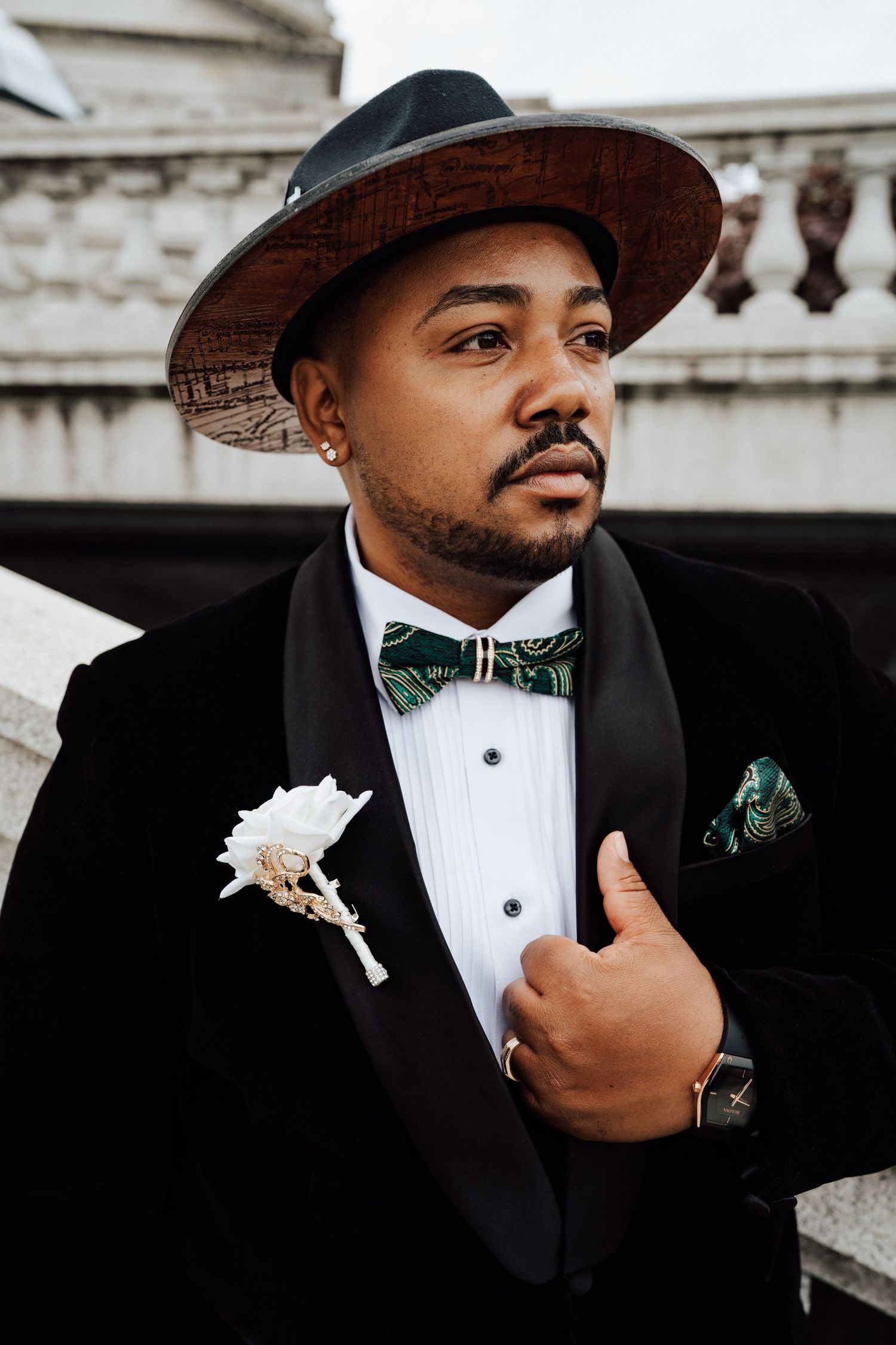 A groom in a black tuxedo and bow tie poses with a white boutonniere with an architectural backdrop at the Harrisburg Capitol Building.