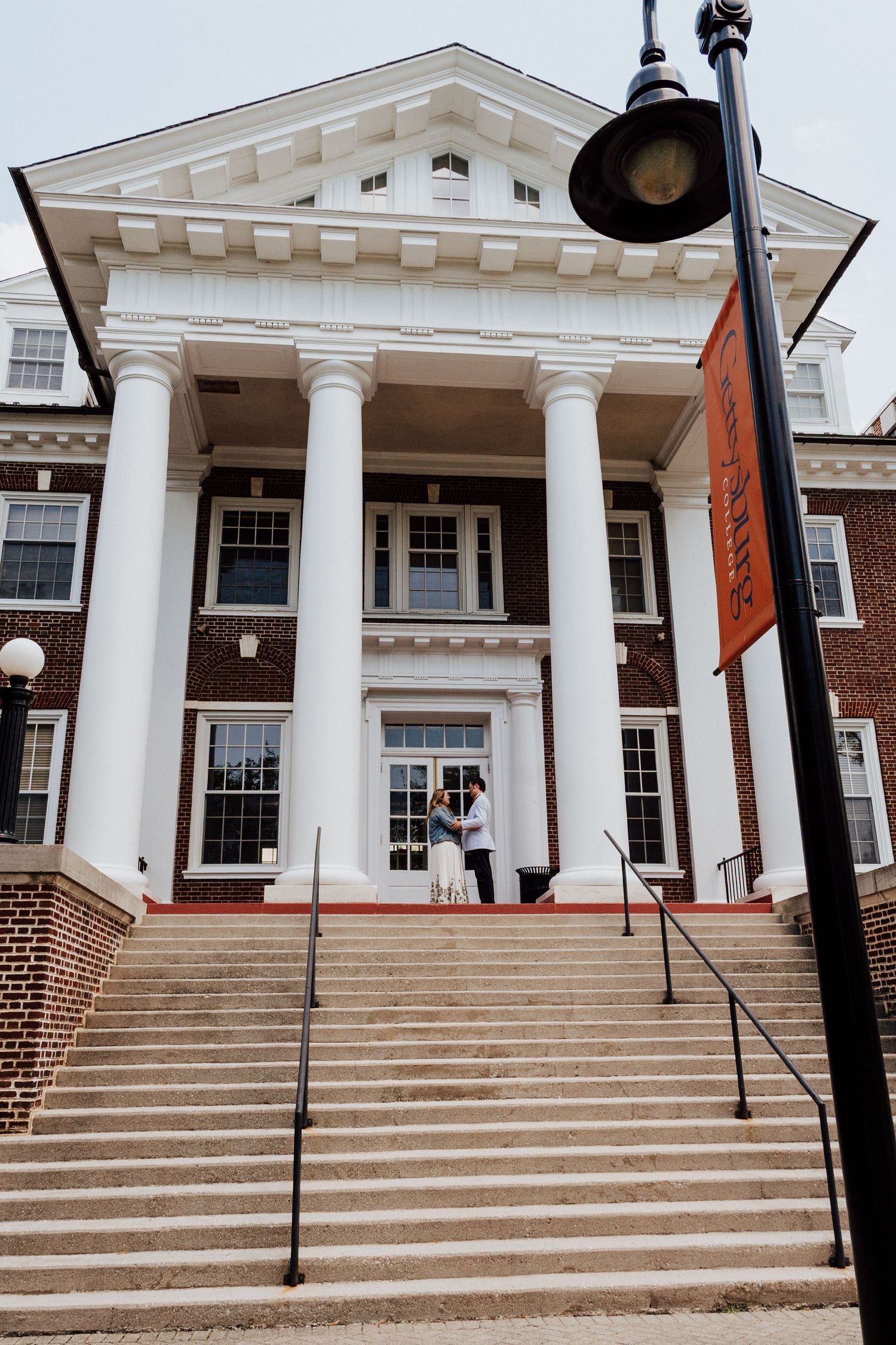 Engaged couple standing in front of building of Gettysburg College, PA for engagement photoshoot.