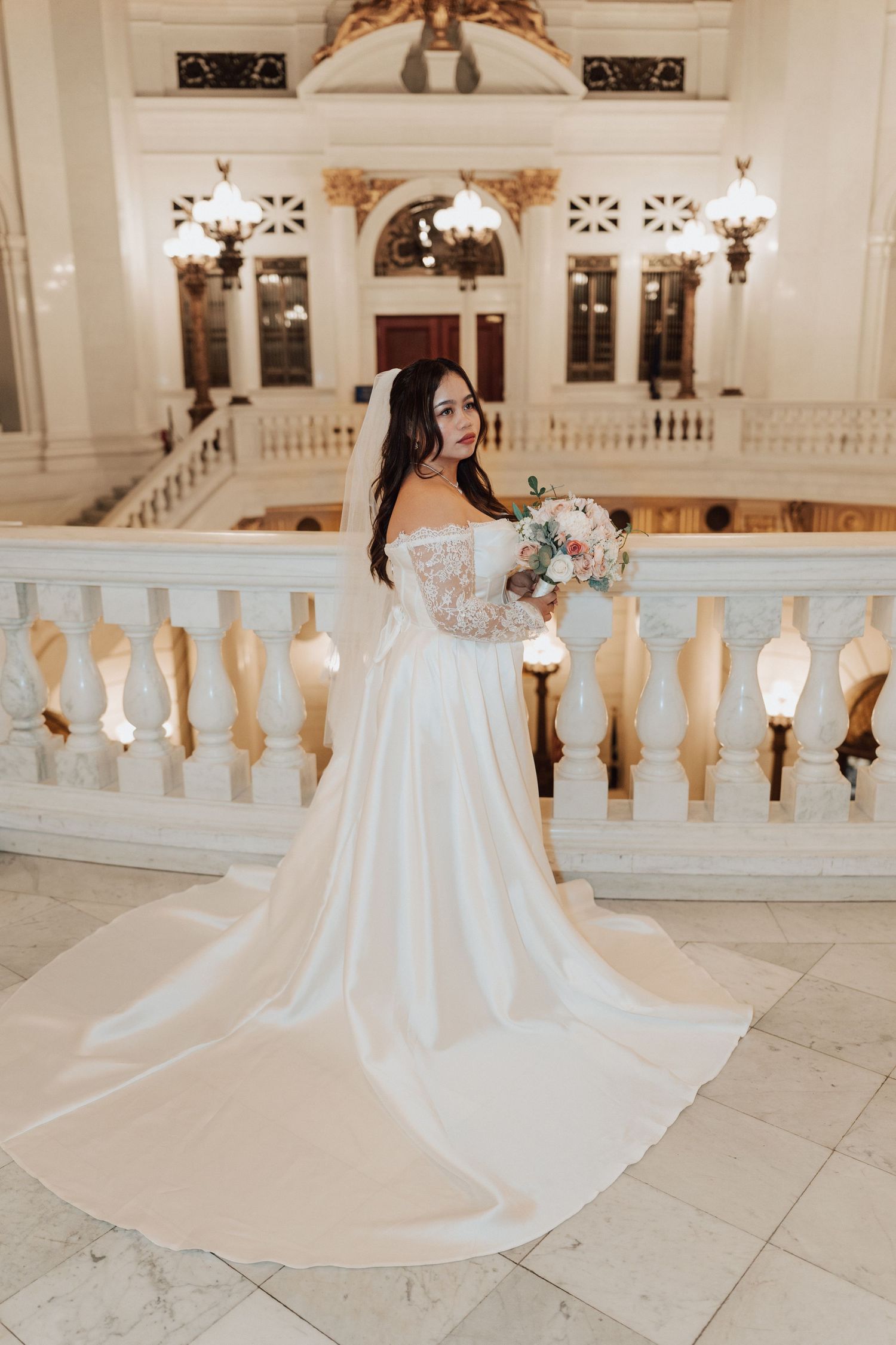 A bride in a flowing white ball gown with long train poses elegantly on at the Harrisburg Capitol Building