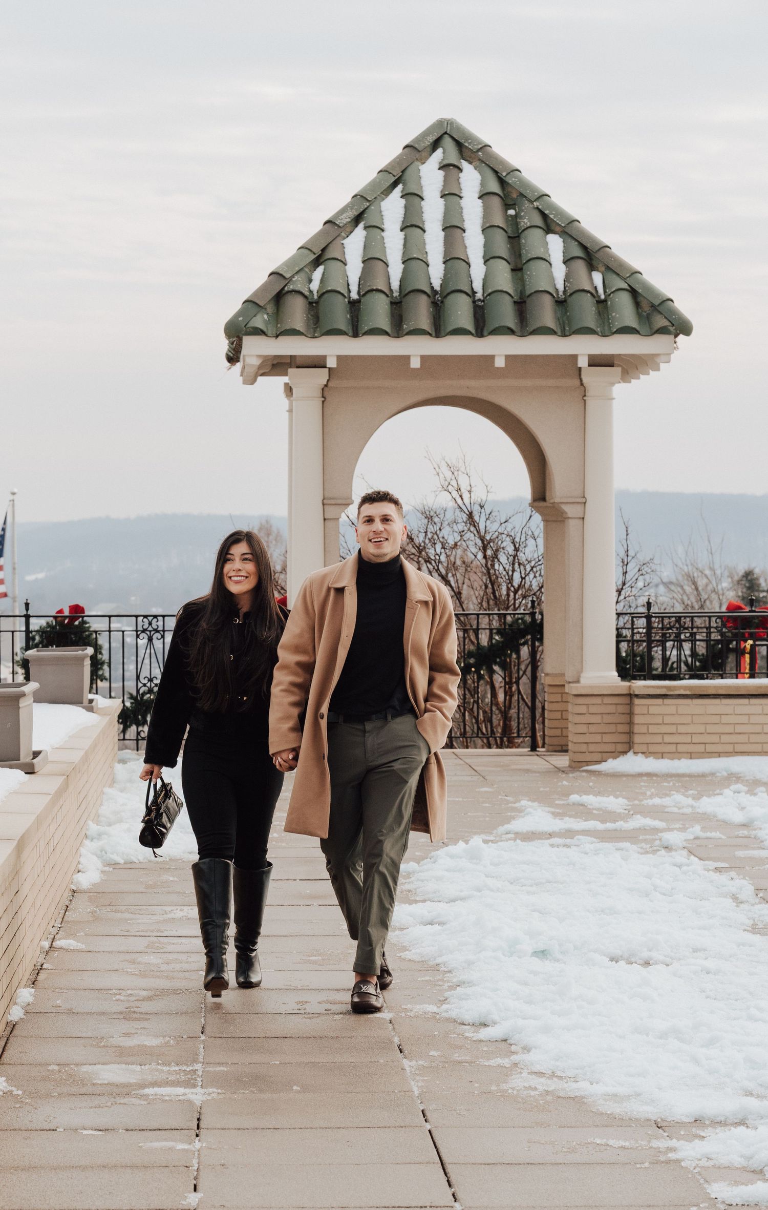 Engaged couple walks at the Hershey Hotel for engagement proposal photoshoot in black and tan outfits for fall and winter.