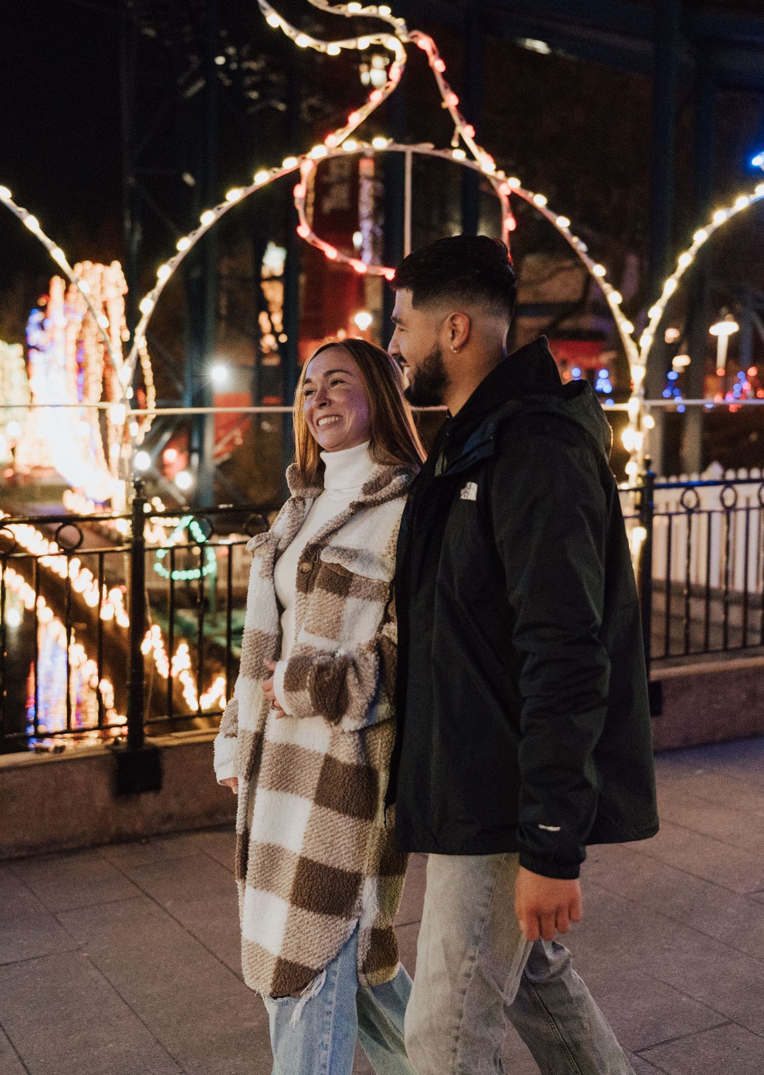 Engaged couple smiling while walking with holiday lights for engagement proposal photoshoot at Hershey Park in Hershey PA