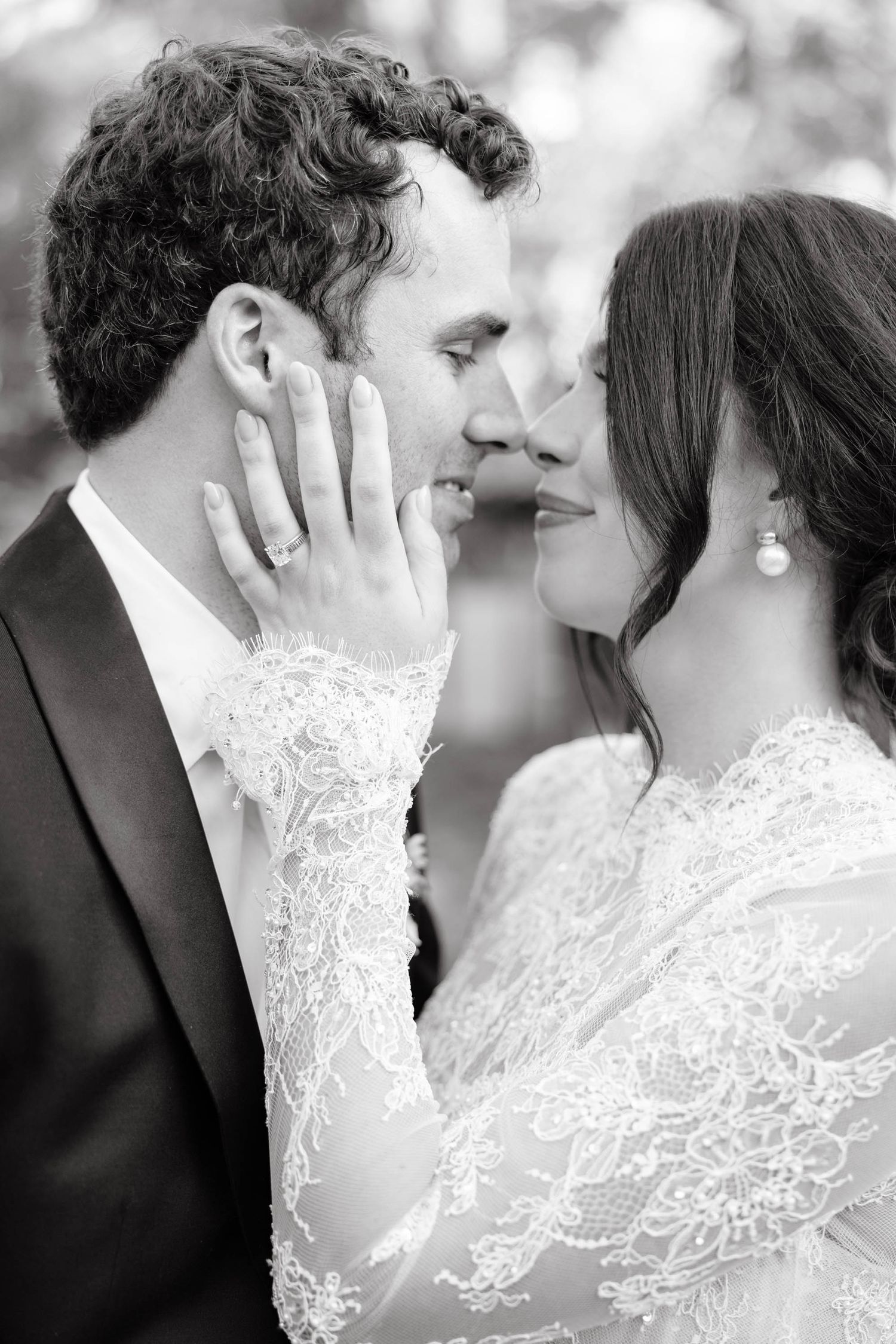 Black and white wedding photo of bride and groom sharing a romantic almost-kiss, bride wearing lace dress and pearl earring.