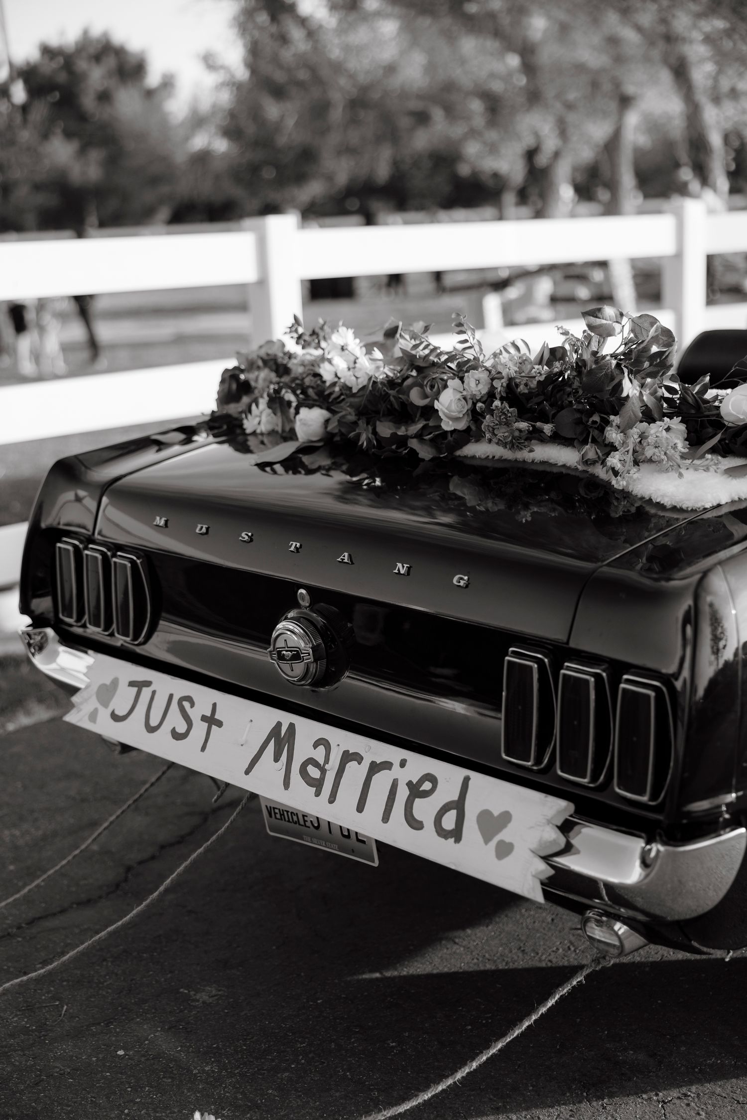 Black and white photo of a classic Ford Mustang with Just Married sign and floral arrangement on trunk.
