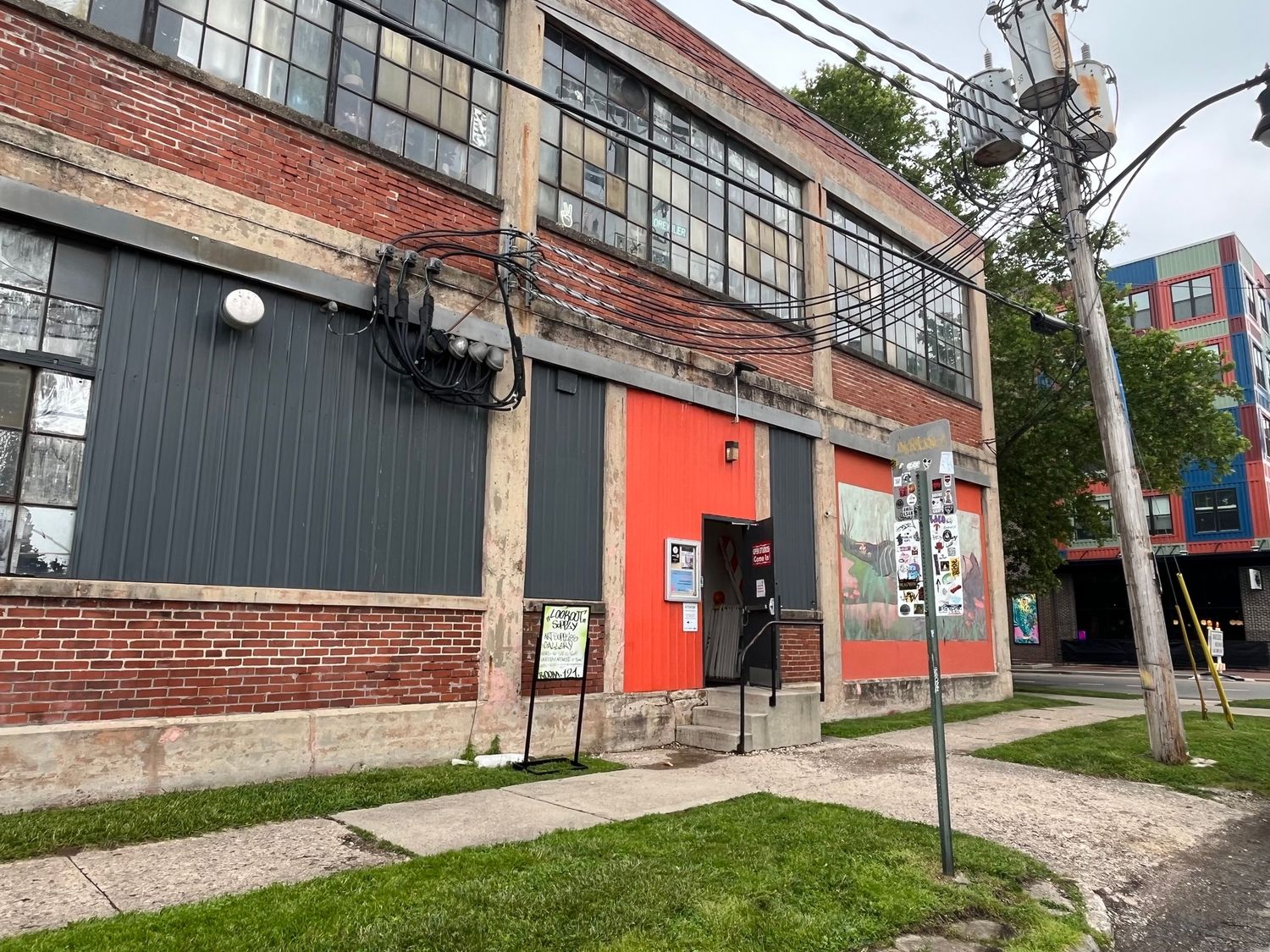 Historic brick industrial building with large windows, red accents, and a sidewalk in an urban neighborhood.