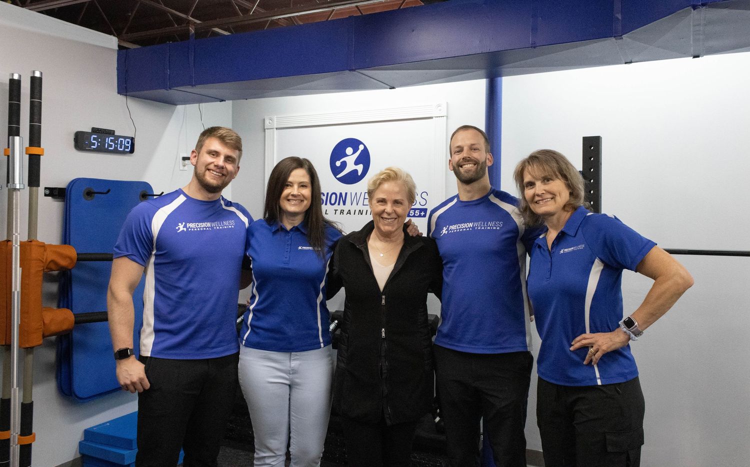 Group of five fitness trainers in blue uniforms posing together inside a training facility.