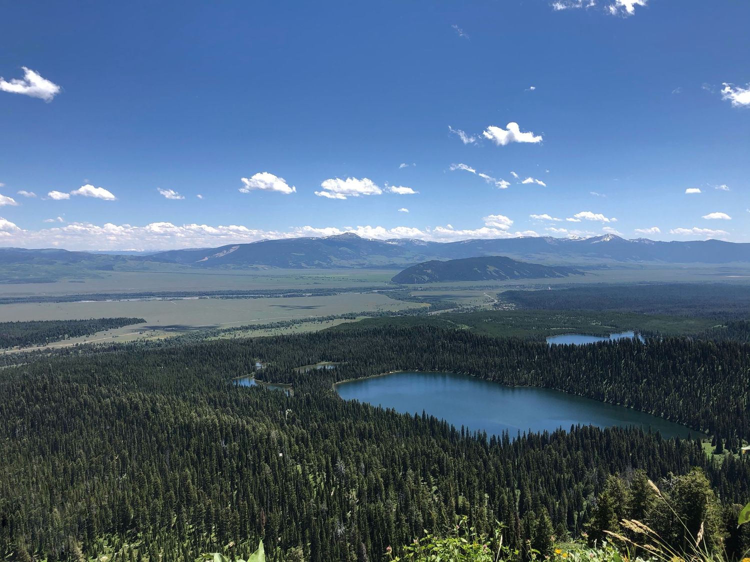 Stunning aerial view of the pristine mountain lake atop the Grand Teton in Wyoming surrounded by dense evergreen forest and distant peaks.