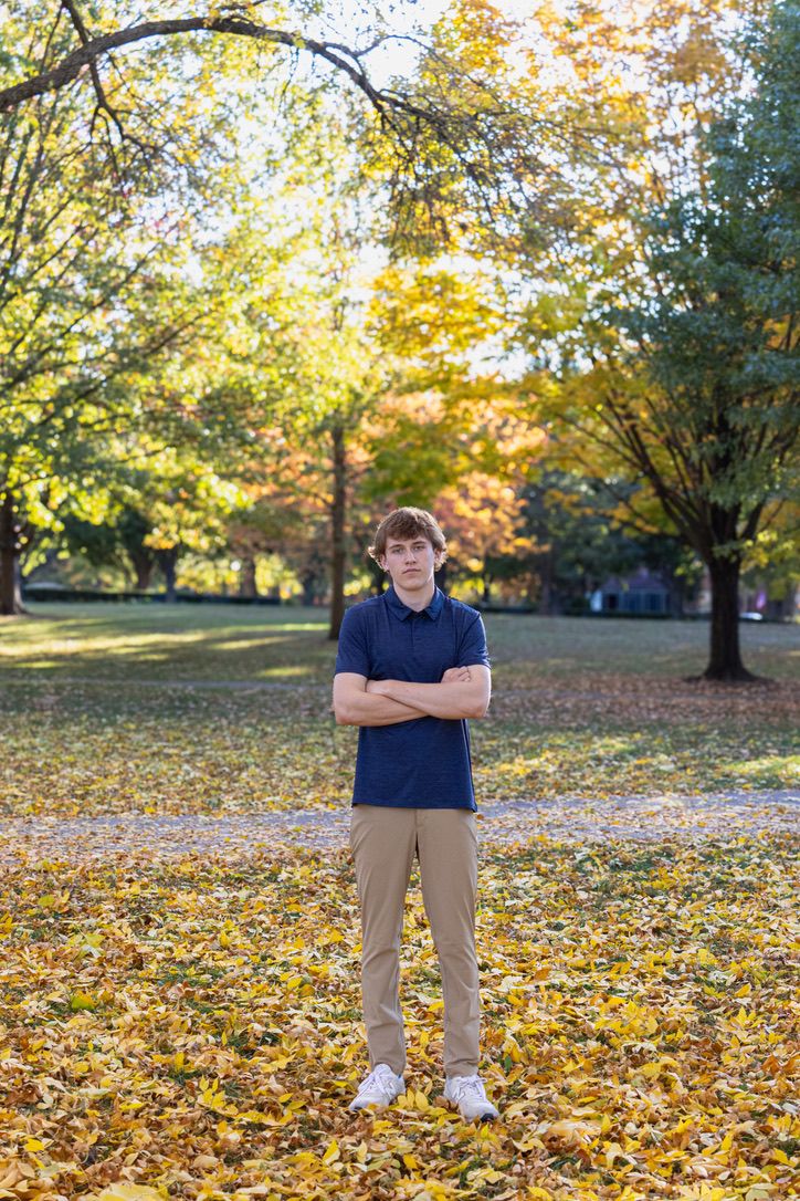 Young man with arms crossed standing in autumn park covered with fallen yellow leaves.