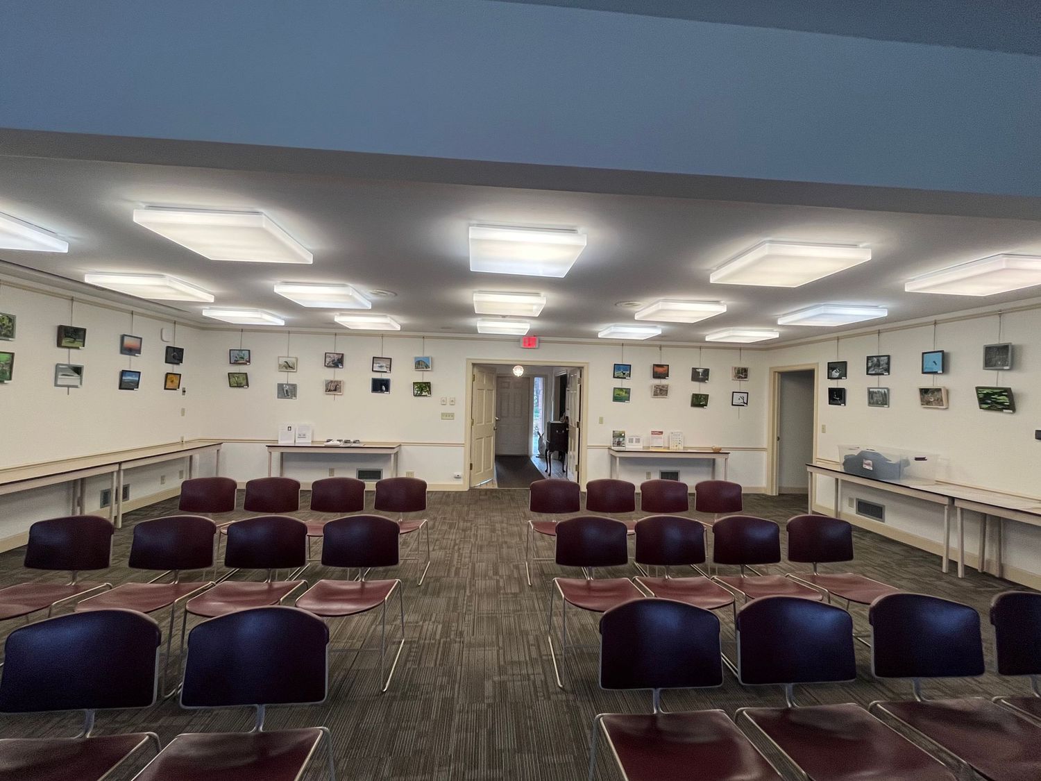 Spacious conference room with rows of purple chairs, artwork on white walls, and recessed lighting panels in the ceiling.