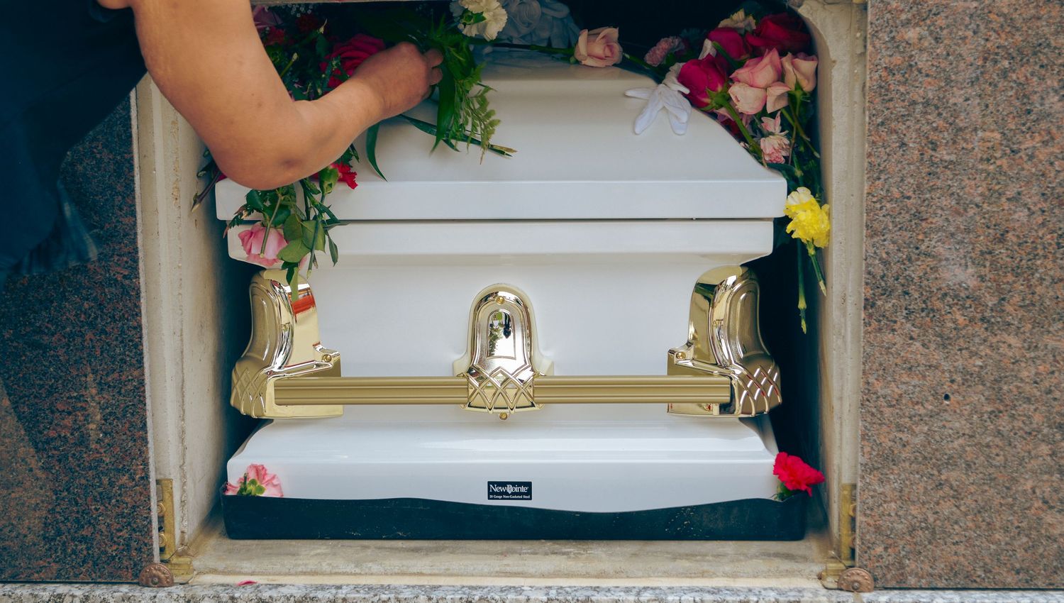 Photo of a white casket in a crypt with a person placing flowers inside.