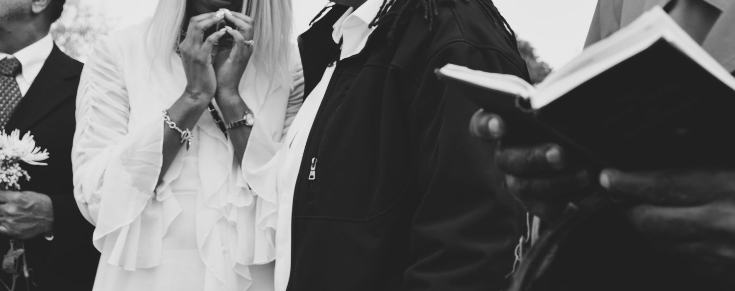 Grayscale photo of a family at a photo and the priest reading a scripture from the Bible.