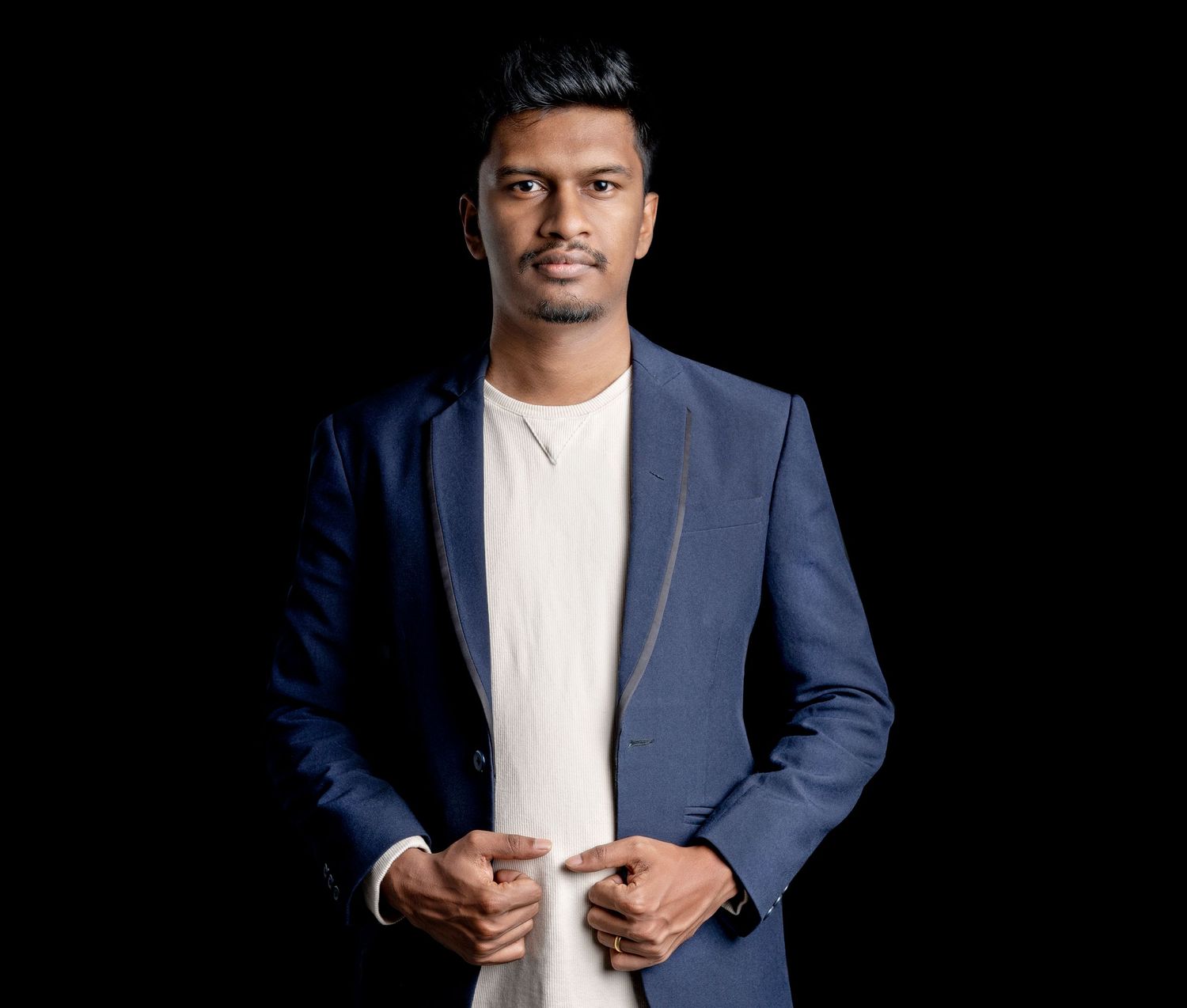 Professional studio portrait against black background featuring navy blazer and white shirt.