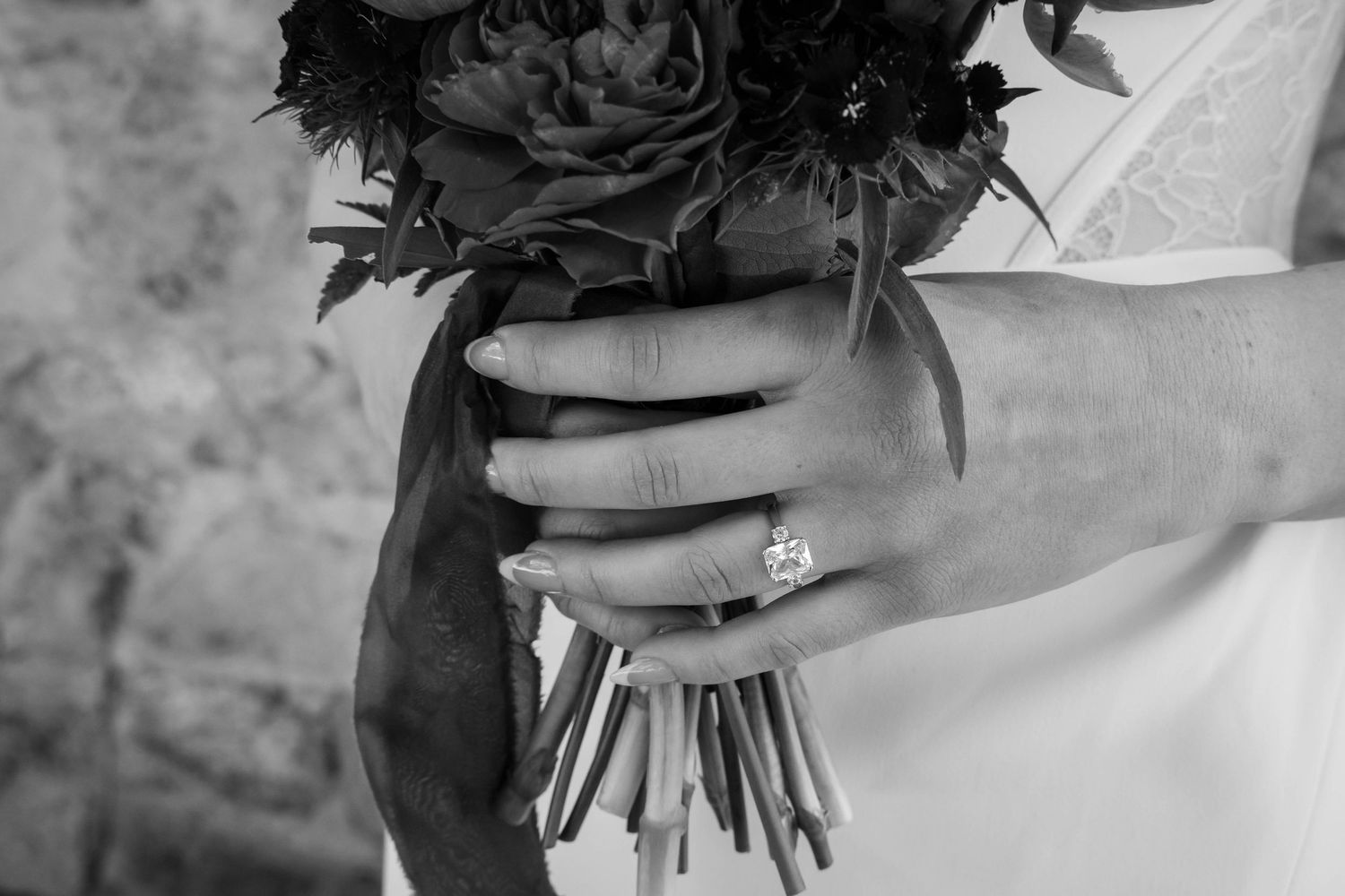 Black and white photo of a bride holding a dark floral bouquet, showcasing an elegant diamond engagement ring.