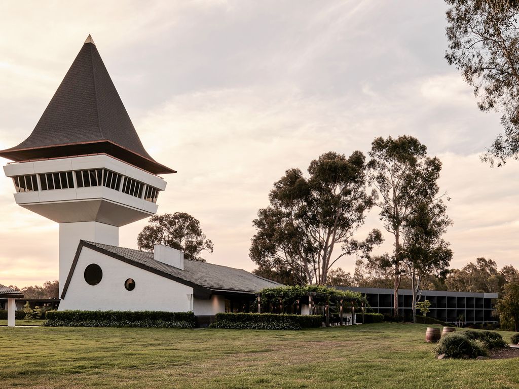 Unique architectural building with tall pointed tower and boat-shaped structure set against cloudy sky at dusk.