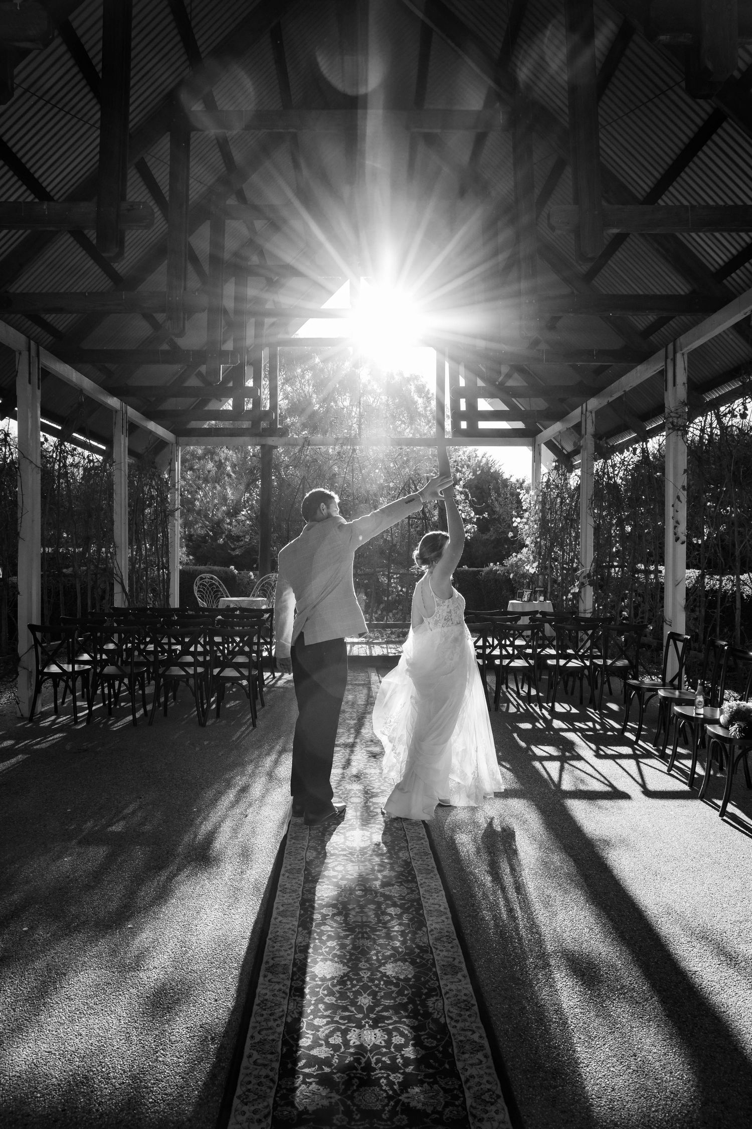Dancing silhouettes beneath a sunlit pavilion cast long shadows across a wooden deck during a special celebration.