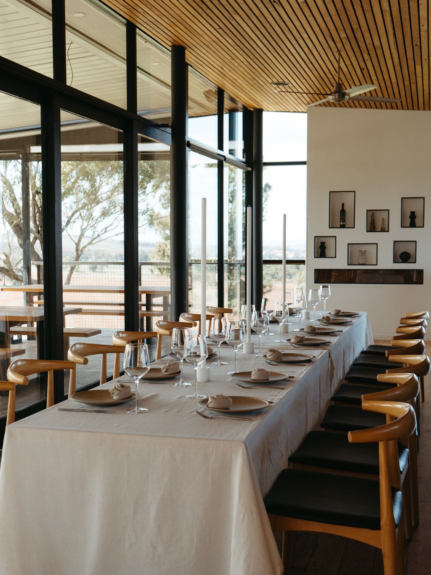 Elegant dining room with long white-clothed table, wooden chairs, floor-to-ceiling windows, and scenic views.