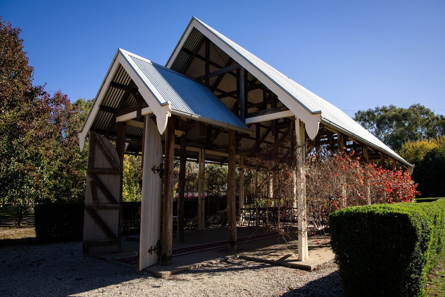 Modern A-frame pavilion with angled wooden beams and stone columns stands surrounded by landscaped gardens.