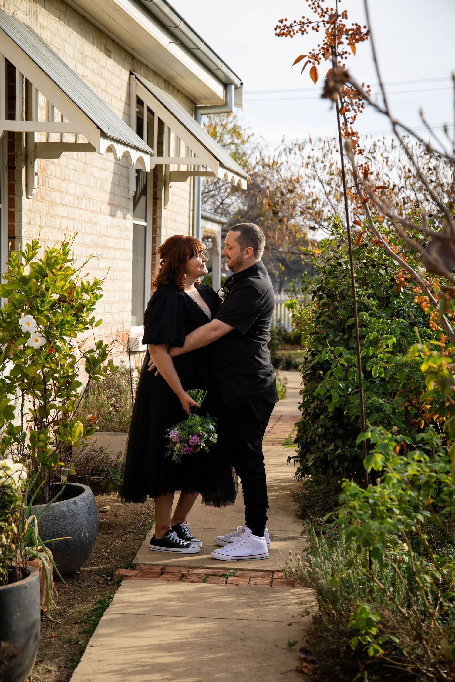 A couple shares tender moments together on their front porch surrounded by potted plants.