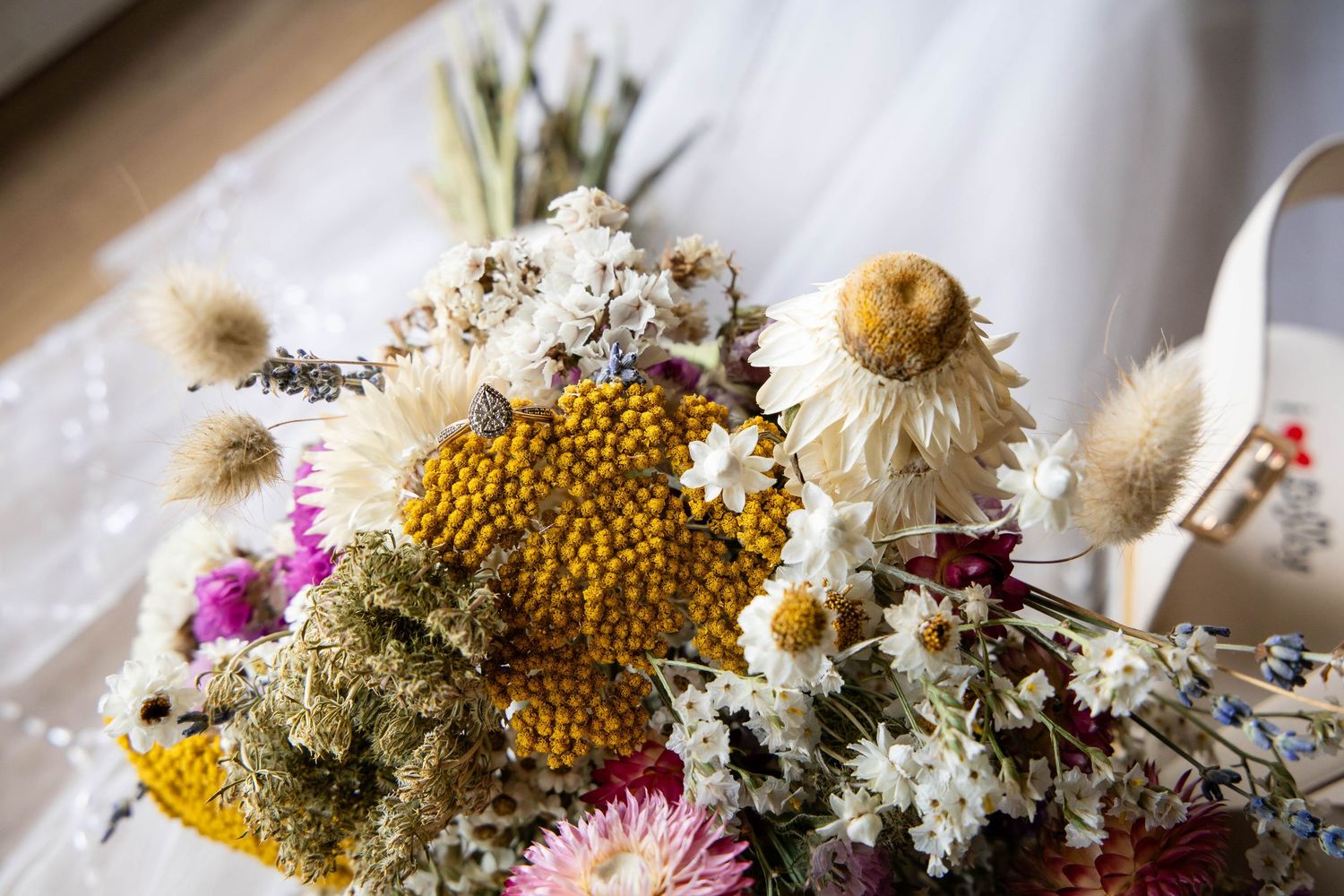 Colorful dried flower bouquet with yellow craspedia, pink strawflowers, white daisies, and fluffy seed heads arrangement.