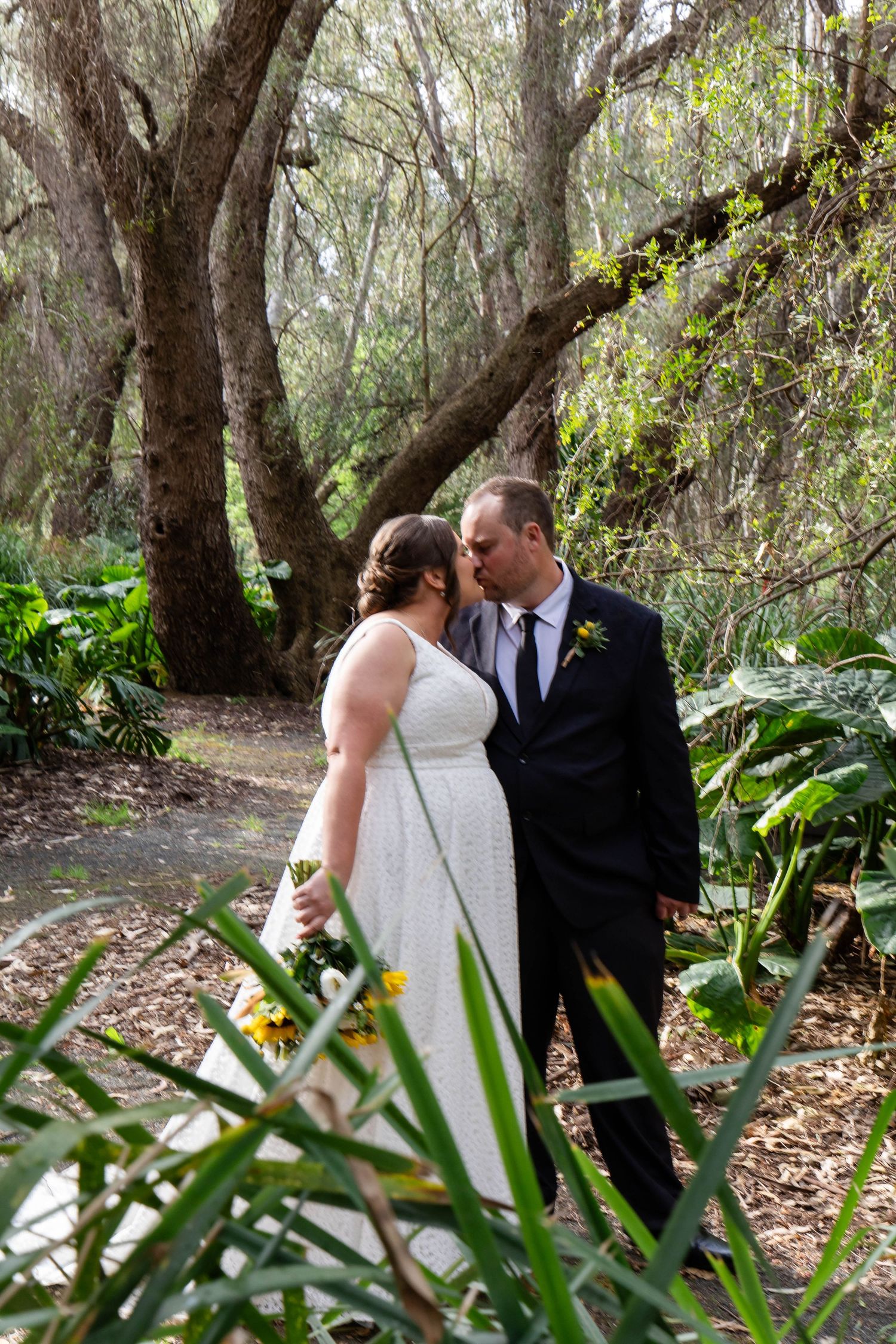 A romantic wedding moment captured between a couple in a lush wooded setting with natural sunlight filtering through trees.