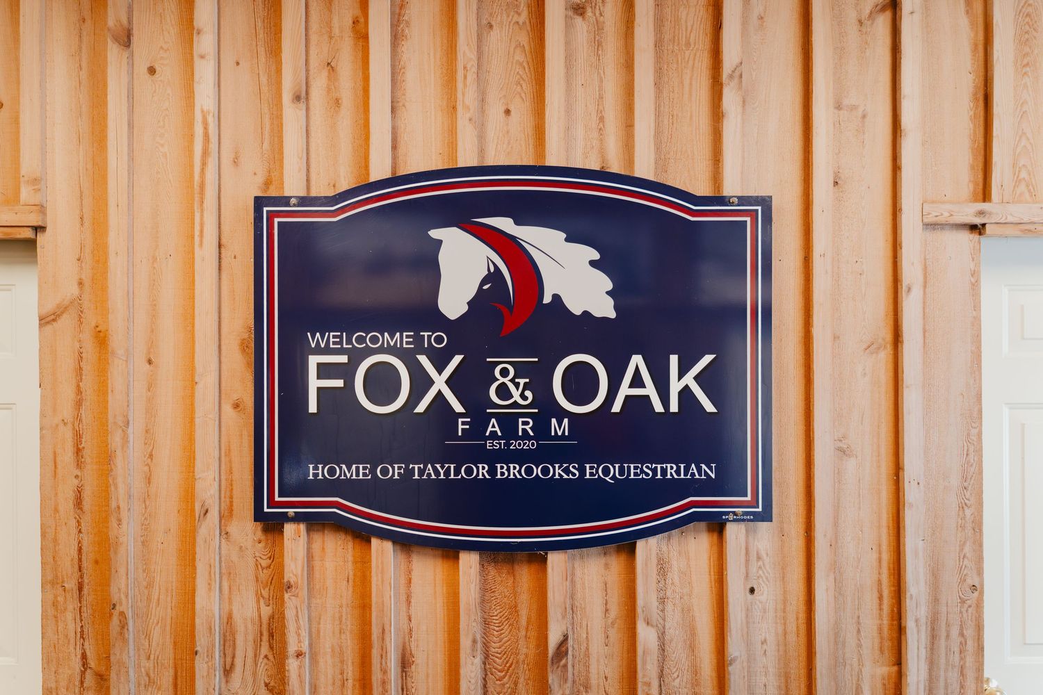 A rustic wooden wall with mounted navy blue and red business signage for Fox & Oak equestrian center.