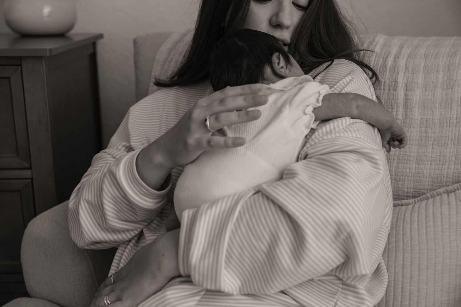 Black and white photo of a woman cradling a newborn baby while sitting on a couch.