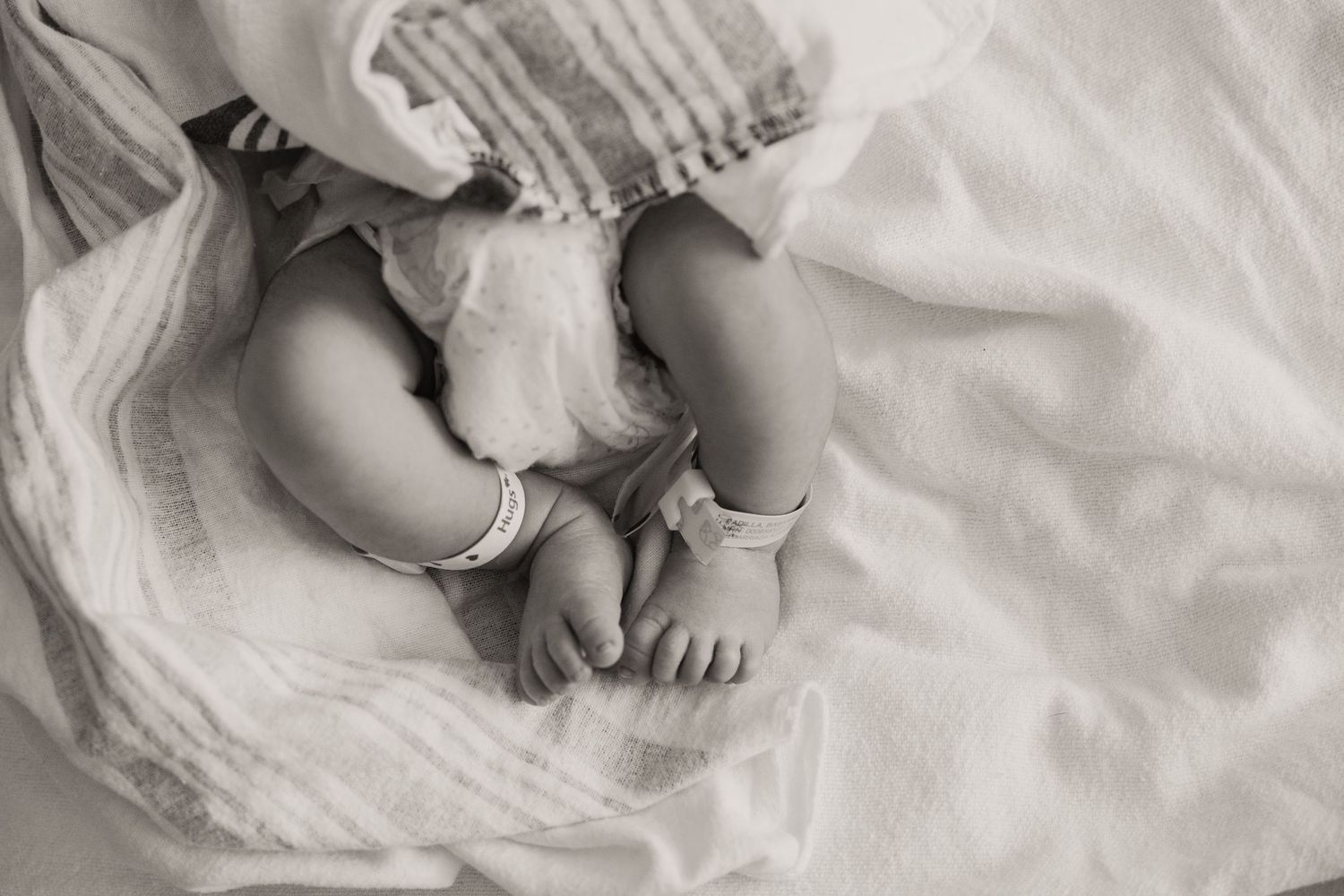 Black and white close-up of newborn baby feet and legs wrapped in soft white textured blanket during Fresh 48 session.