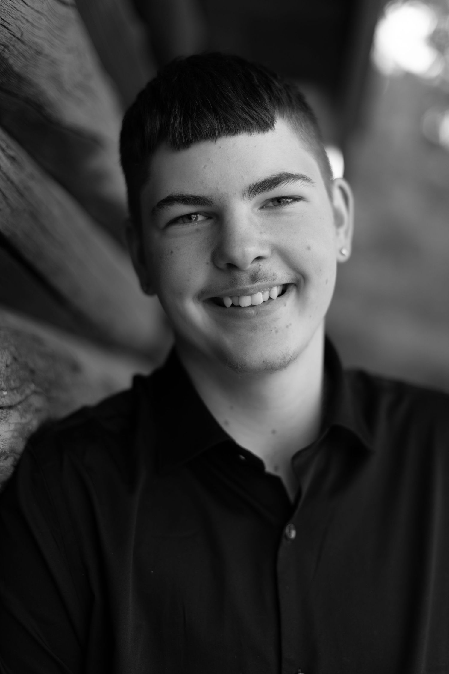 Black and white portrait shot of young man in dark shirt against wooden background.