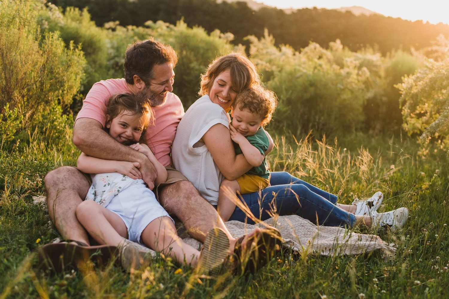 Familia sentada en una lona en el pasto sonriendo, al atardecer