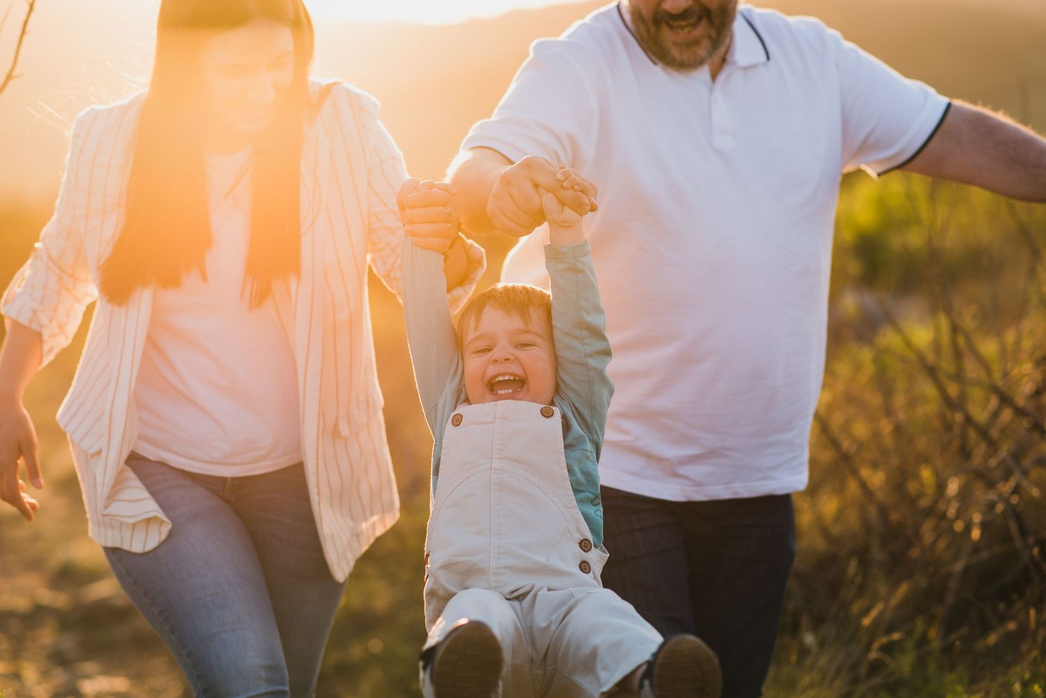 Mamá y Papá hamacando a niño de los brazos durante una sesión de fotos familiar en tandil
