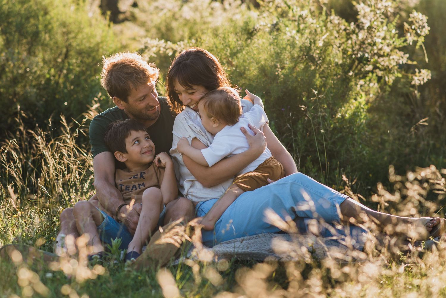 Familia sentada en una lona mirándose y sonriendo durante una sesión de fotos familiar en tandil
