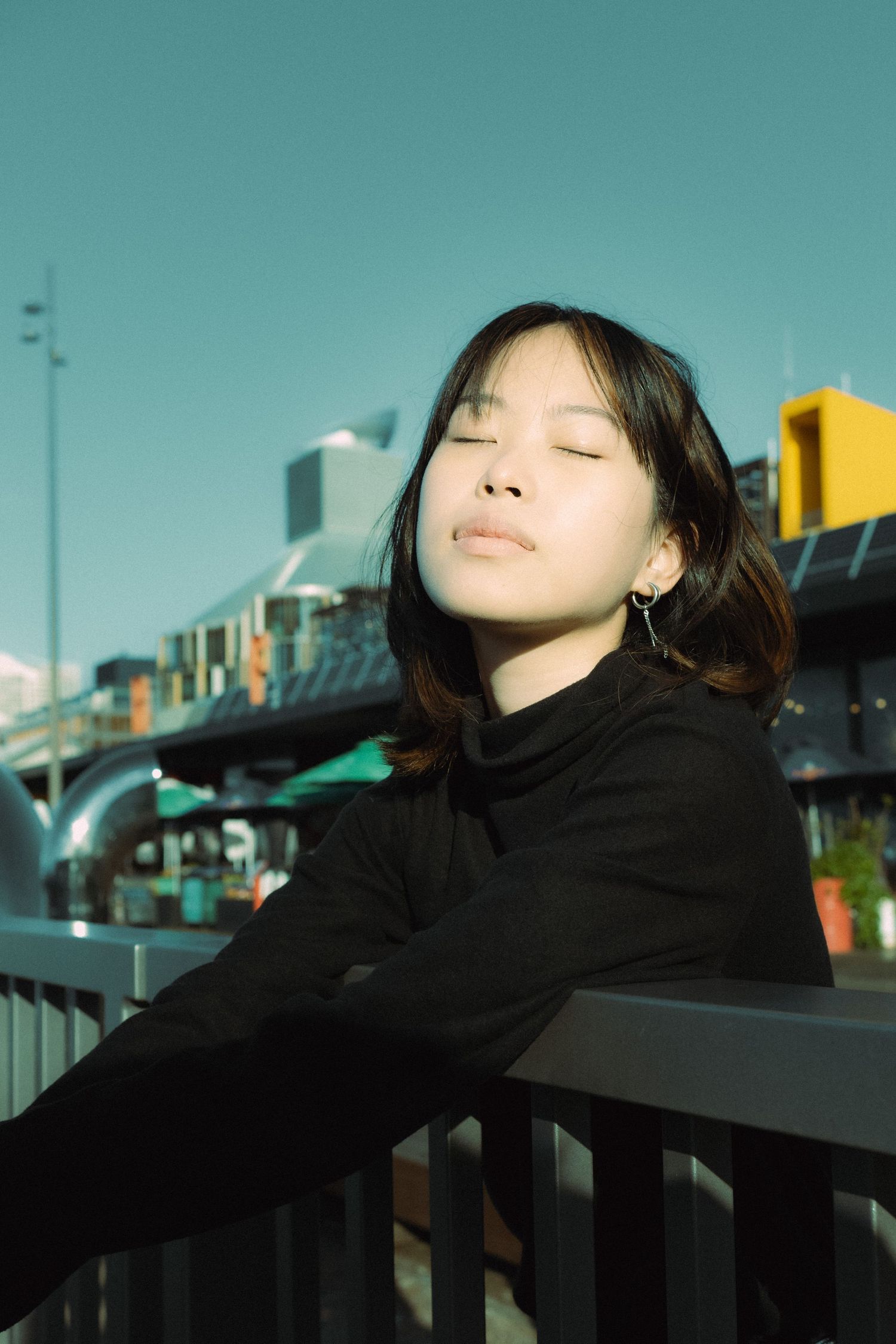 Asian model leaning against a rail with her eyes closed, getting sun kissed.