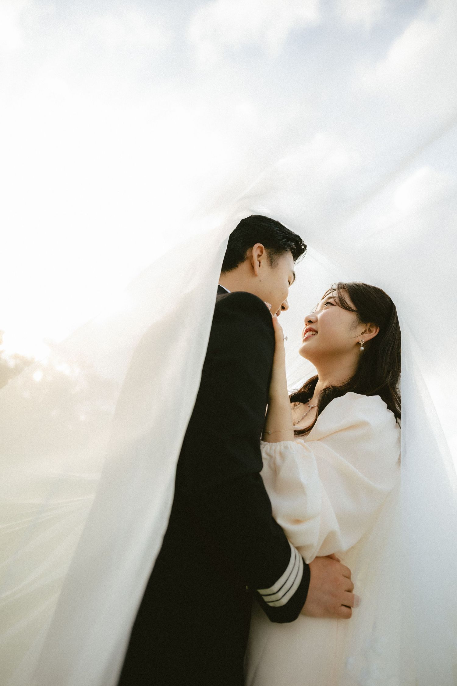 A romantic couple in black and white clothing embrace tenderly against a soft white background.