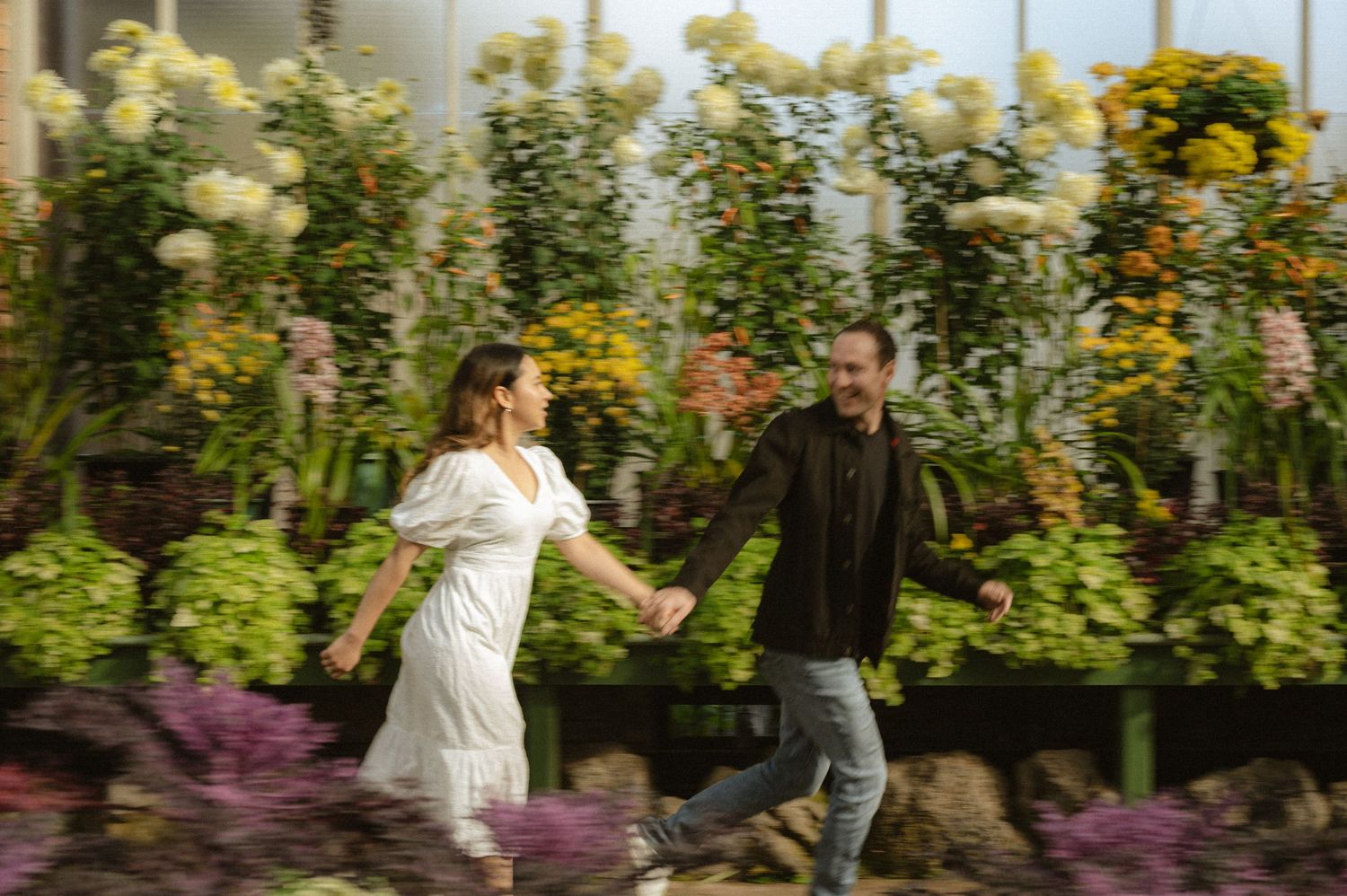 A couple shares a romantic moment in a lush garden setting with vibrant flowers and greenery.