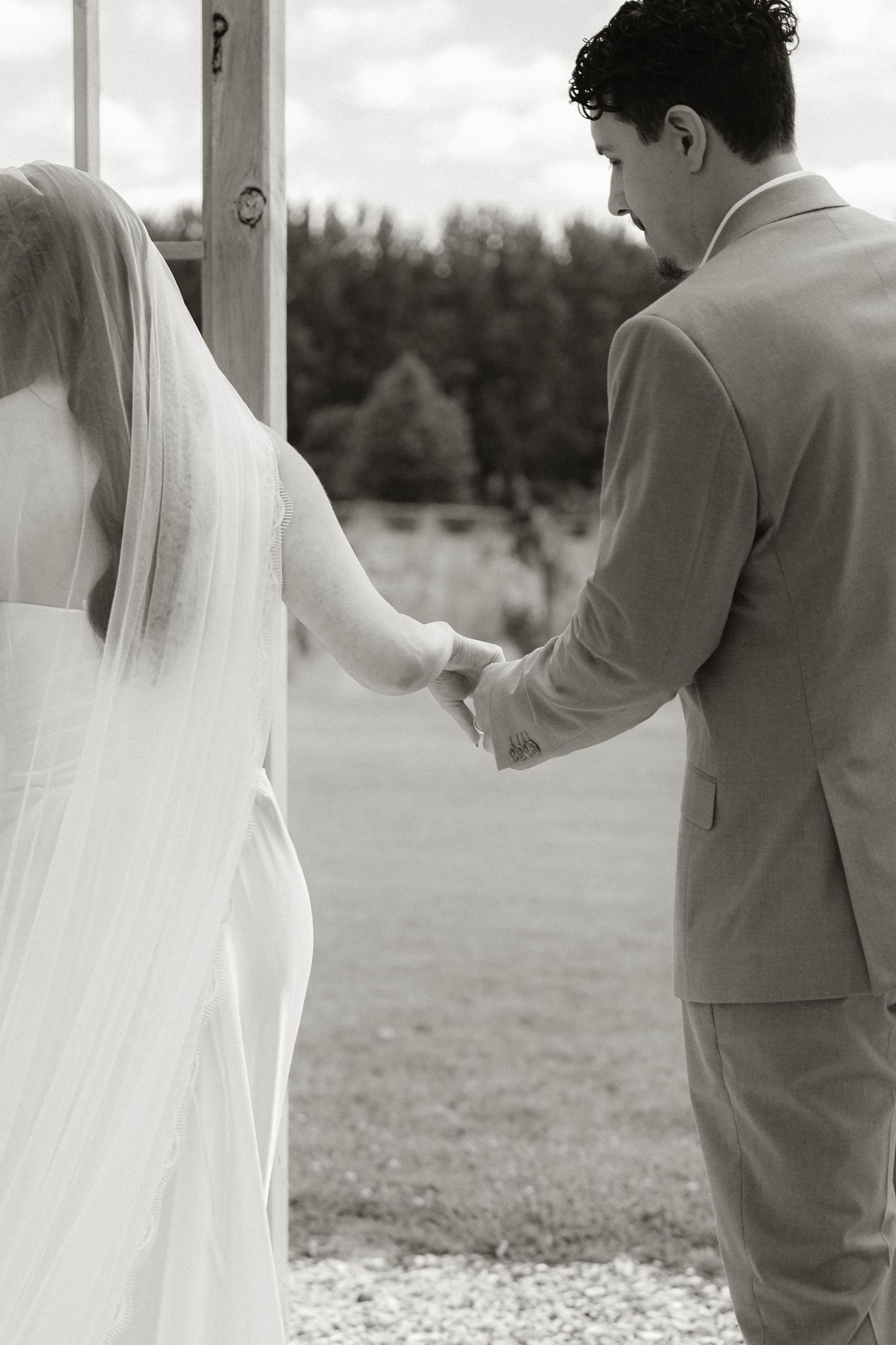 Black and white photo of a bride and groom holding hands at an outdoor wedding ceremony.