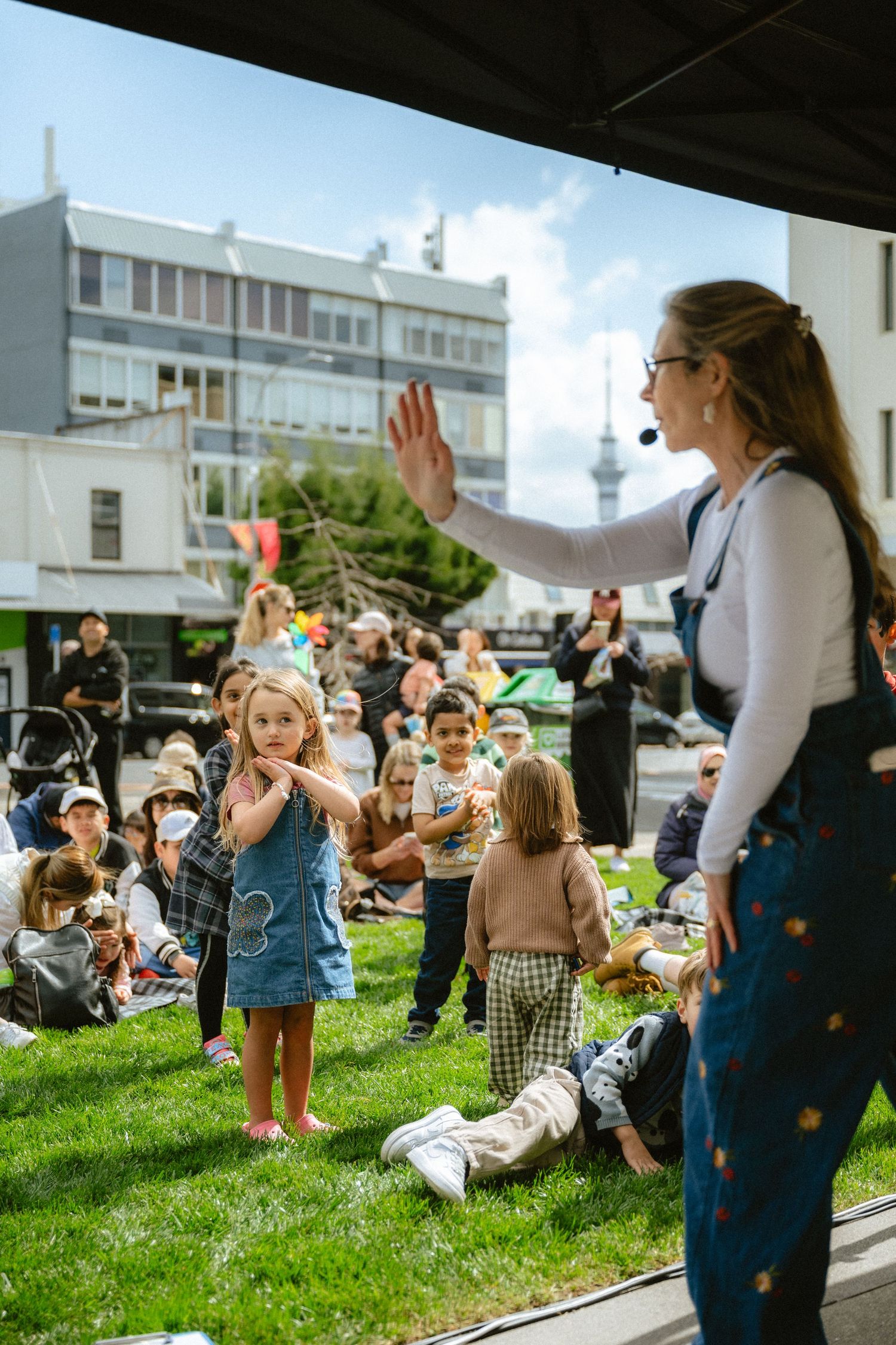 People gather on a grassy lawn for an outdoor event while an instructor leads an activity on a sunny day.