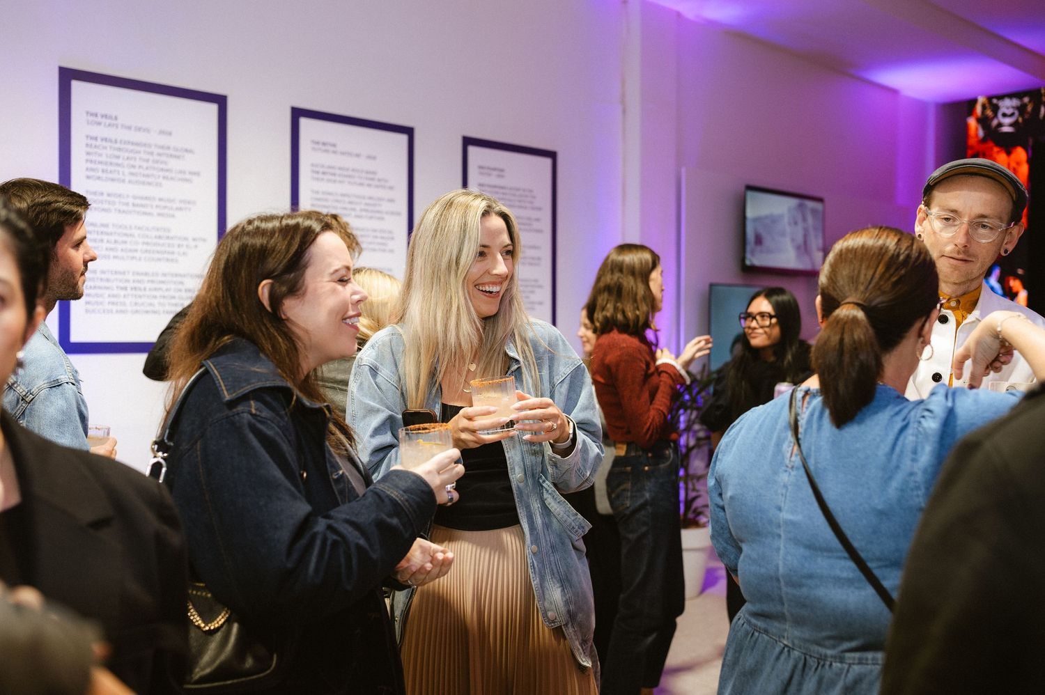 Professional networking event with attendees mingling in a modern space with purple lighting.