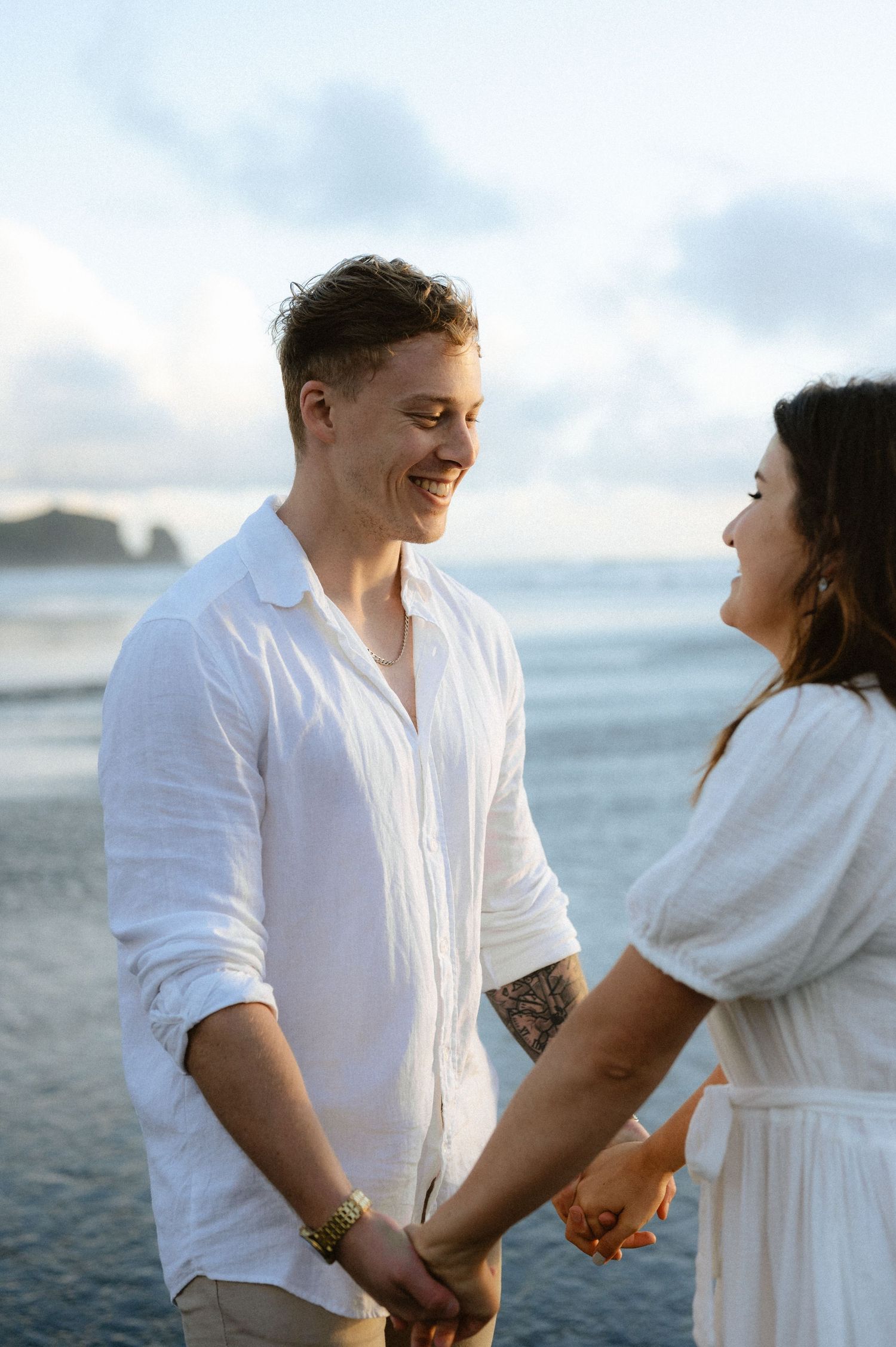 Couple in white clothing shares intimate moments during a beach photoshoot at sunset.