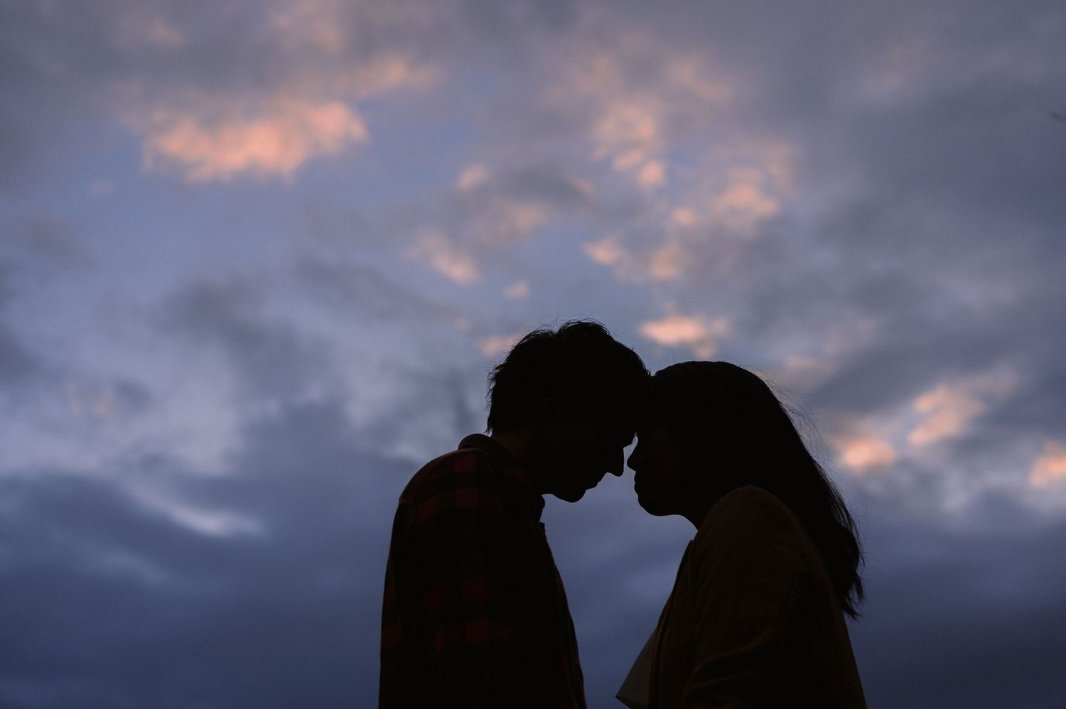 Silhouette of boy and girl forehead to forehead with a beautiful pink and purple sunset behind them.