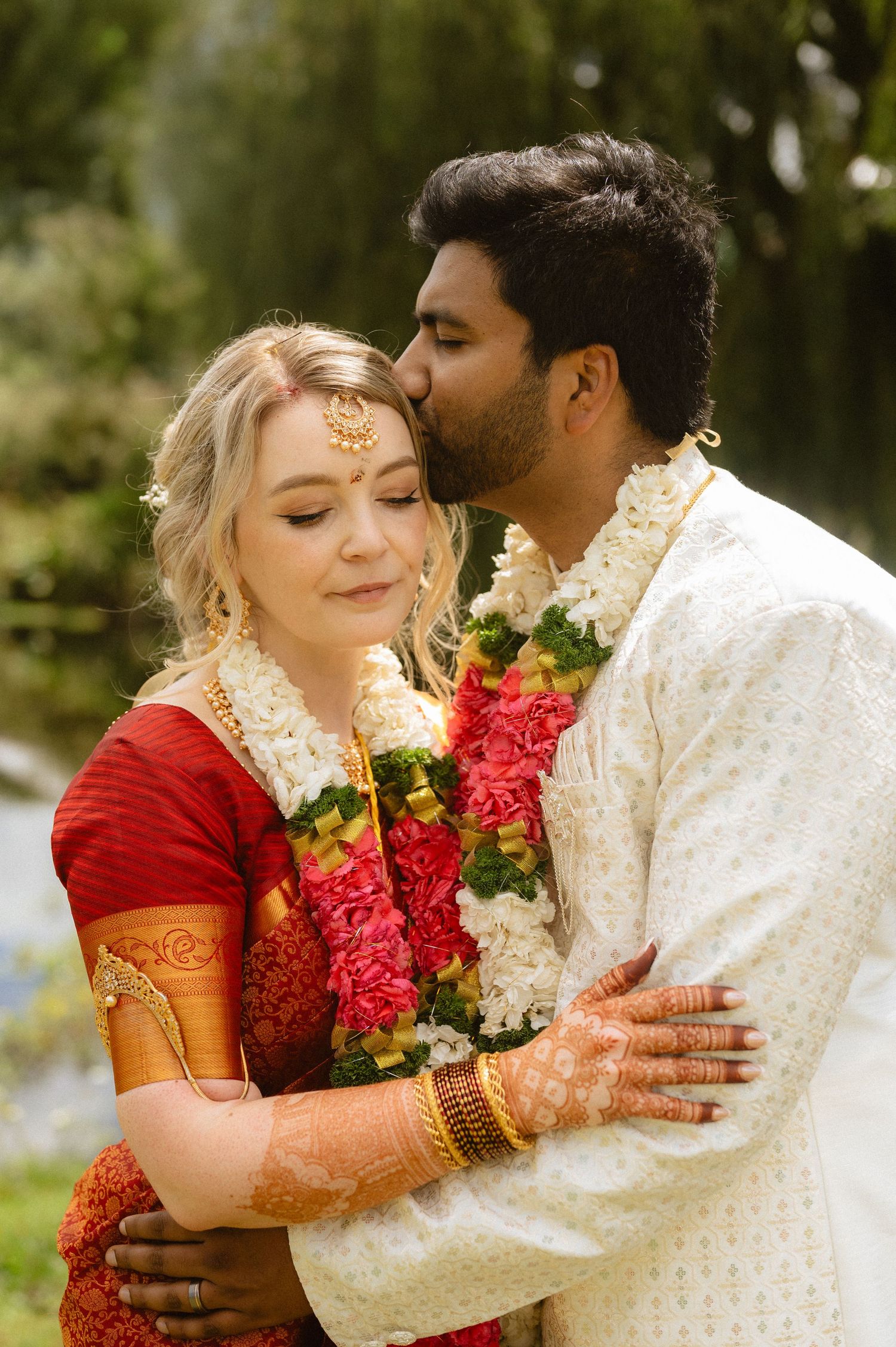Couple in traditional Indian wedding attire share intimate moments during outdoor photo session.