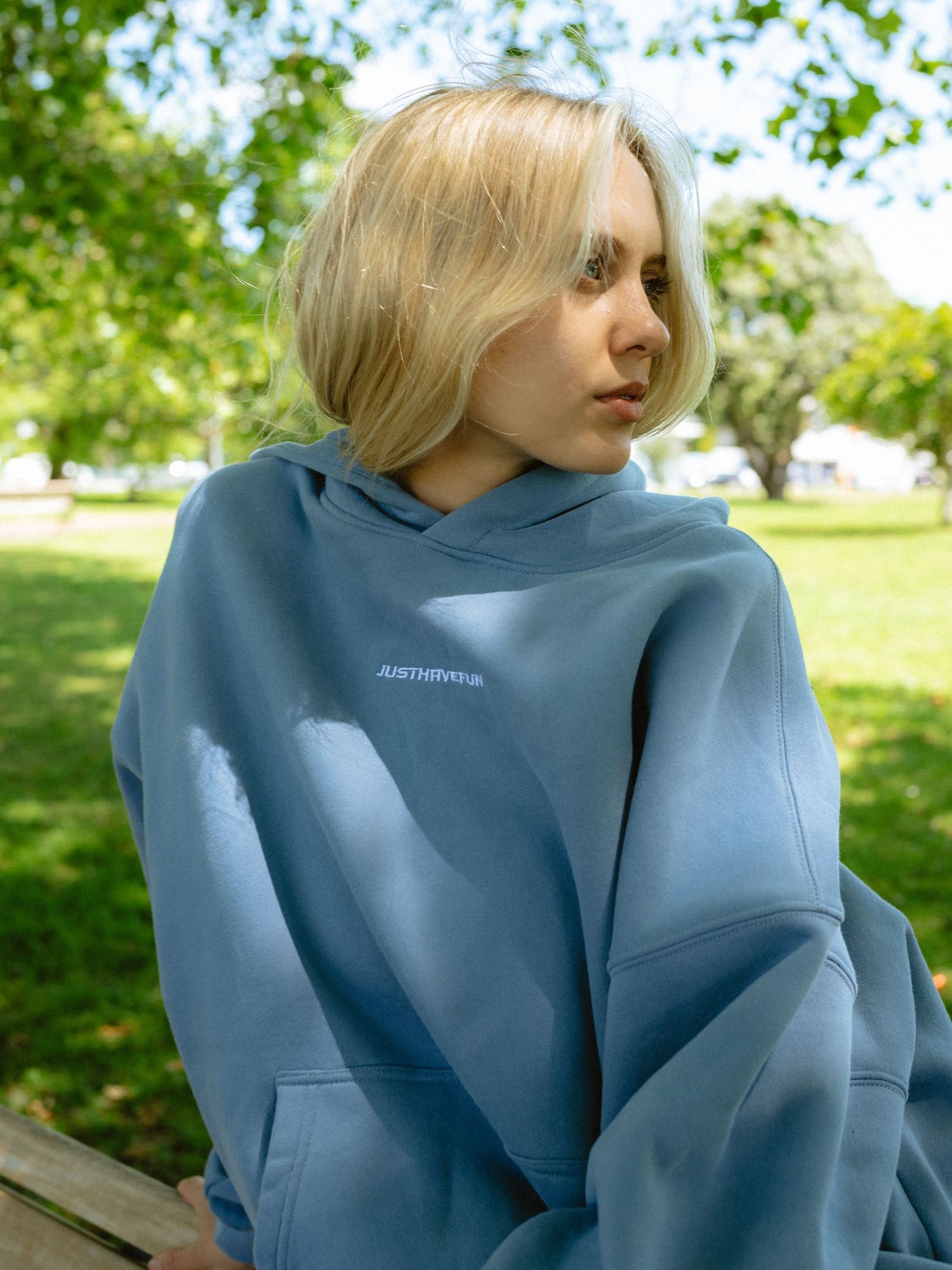 Person wearing a light blue structured jacket poses outdoors in a park setting.