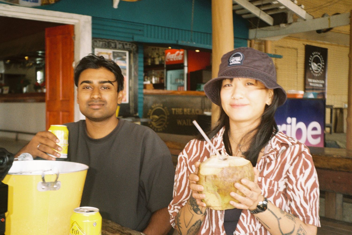 Two friends enjoying tropical drinks at a casual outdoor beach bar restaurant.