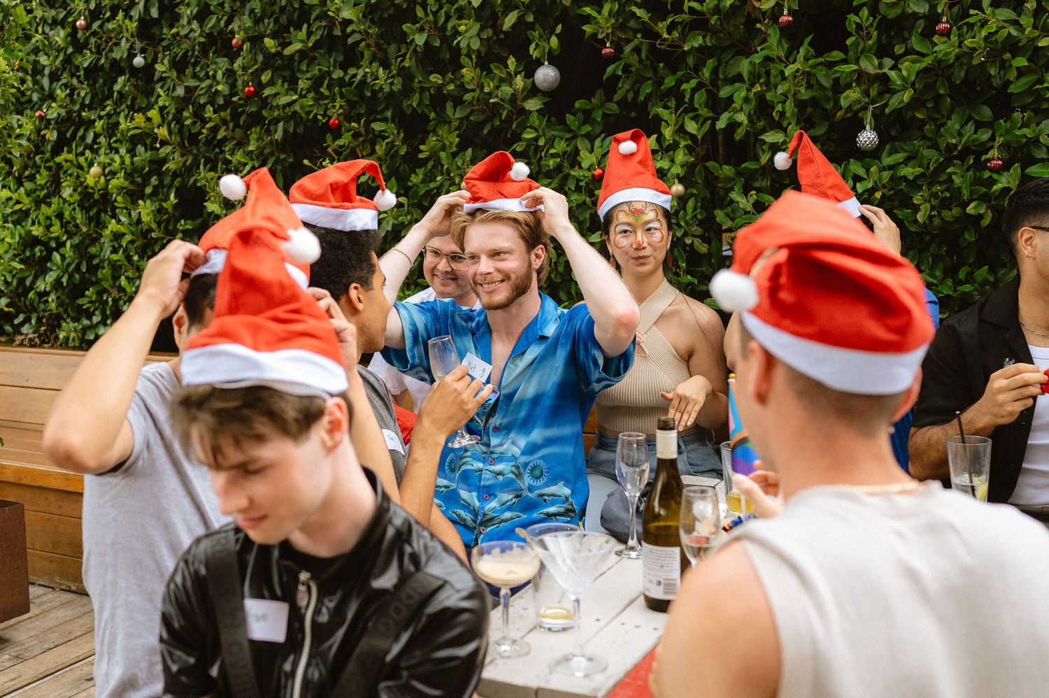 Group wearing Santa hats celebrating at an outdoor holiday gathering.
