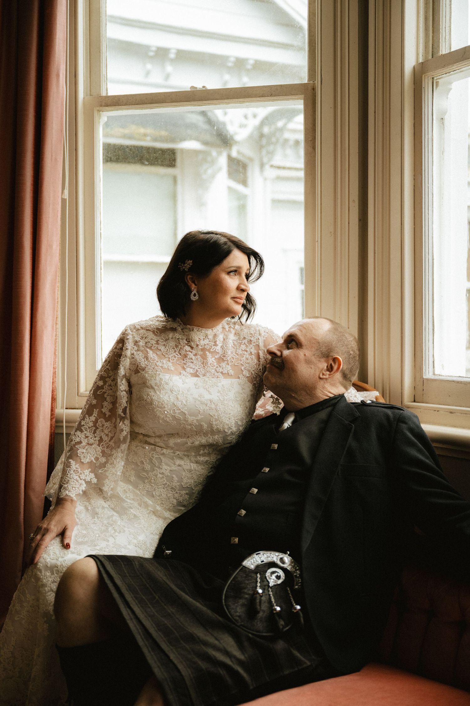 Couple sharing an intimate moment by sunlit windows in vintage setting.