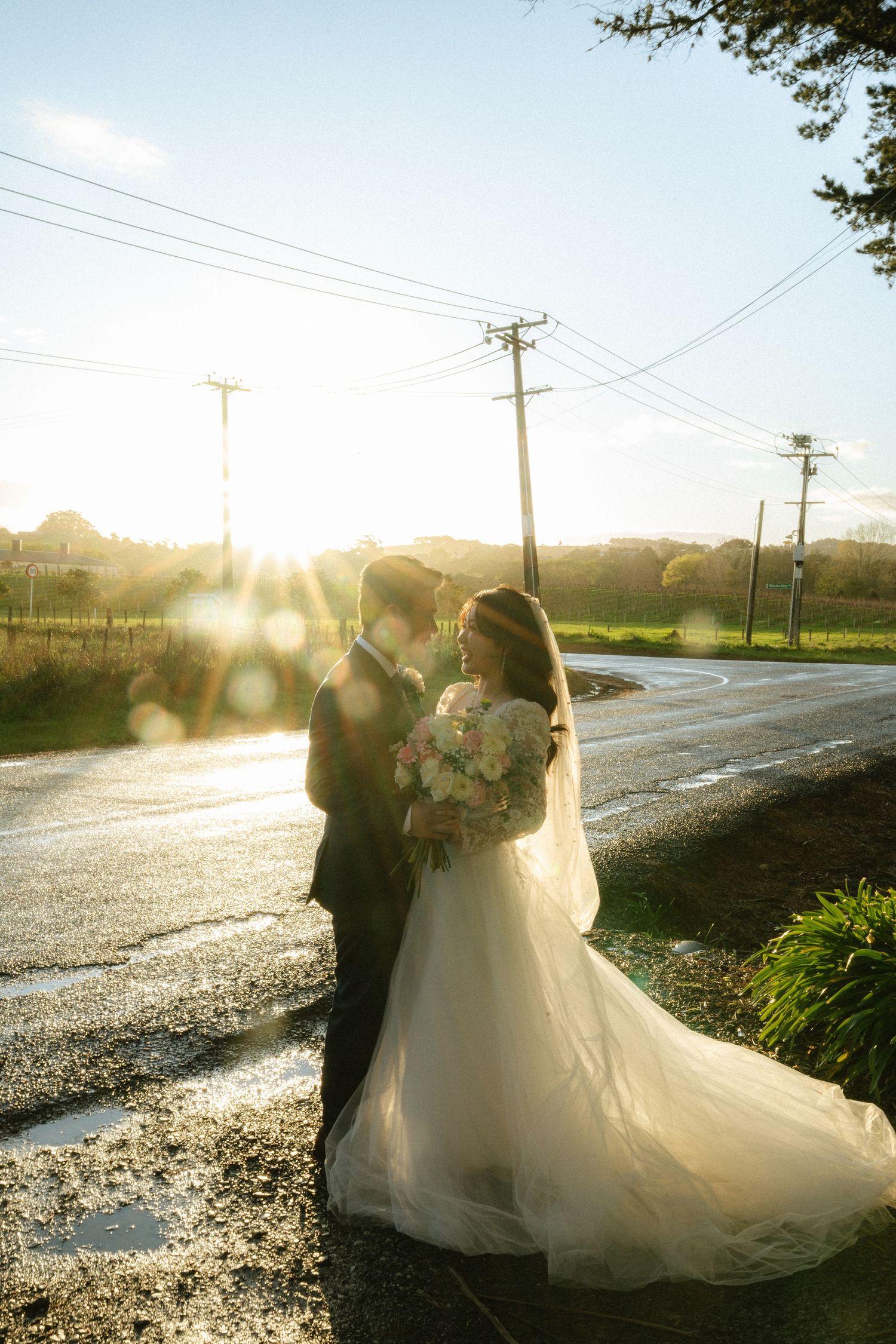 A couple shares a romantic moment at sunset on a country road with golden light streaming through the trees.