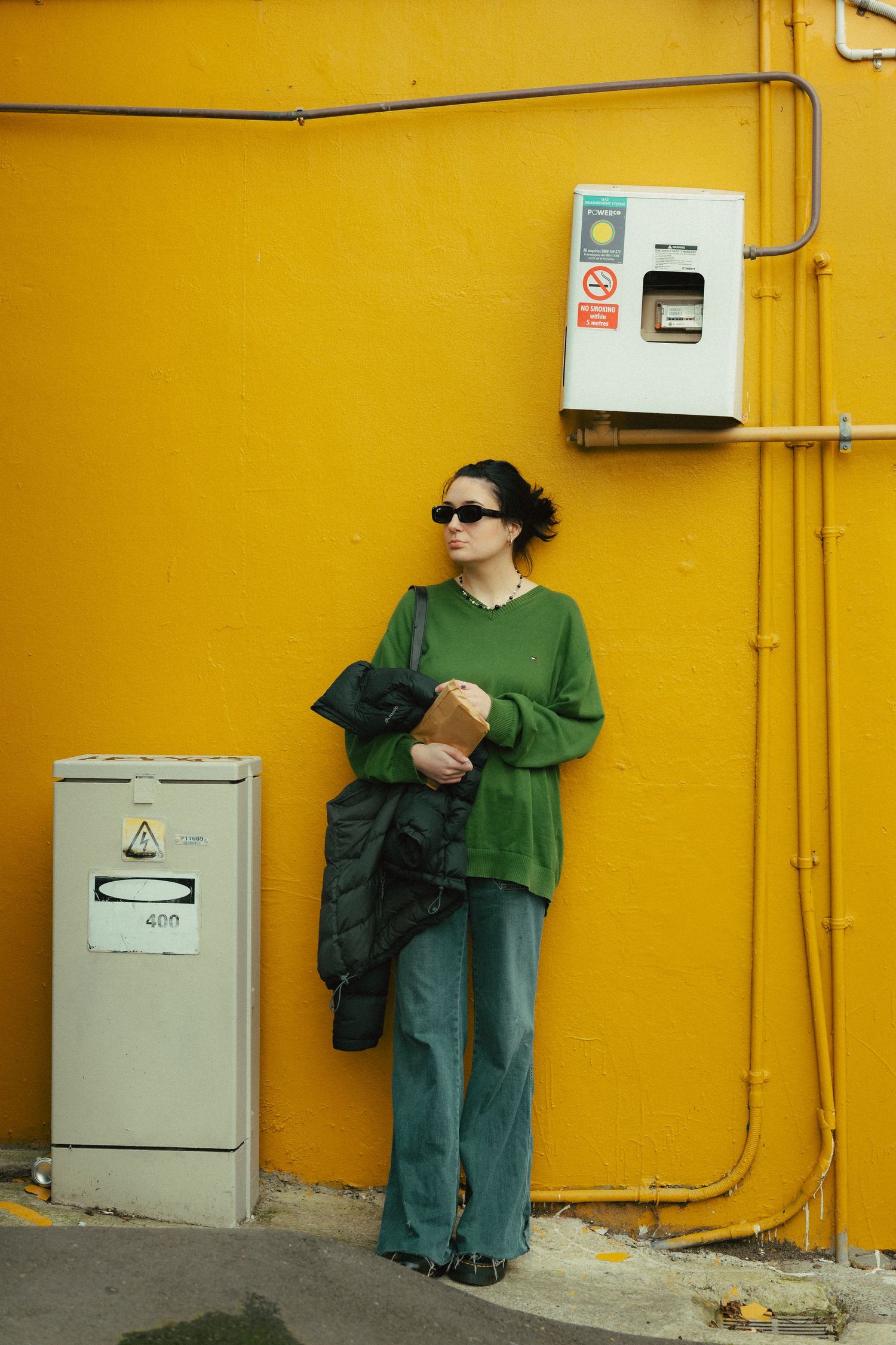 Cool girl wearing green sweater leaning against a mustard yellow wall.
