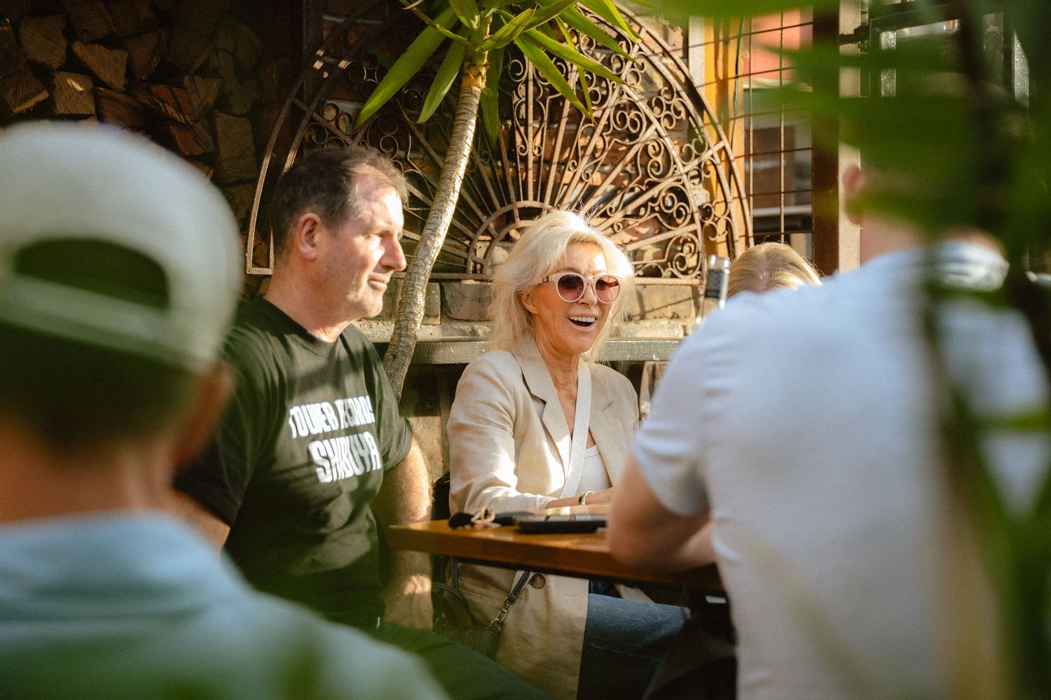 A person laughs joyfully while dining at a restaurant with warm lighting and natural greenery in the background.