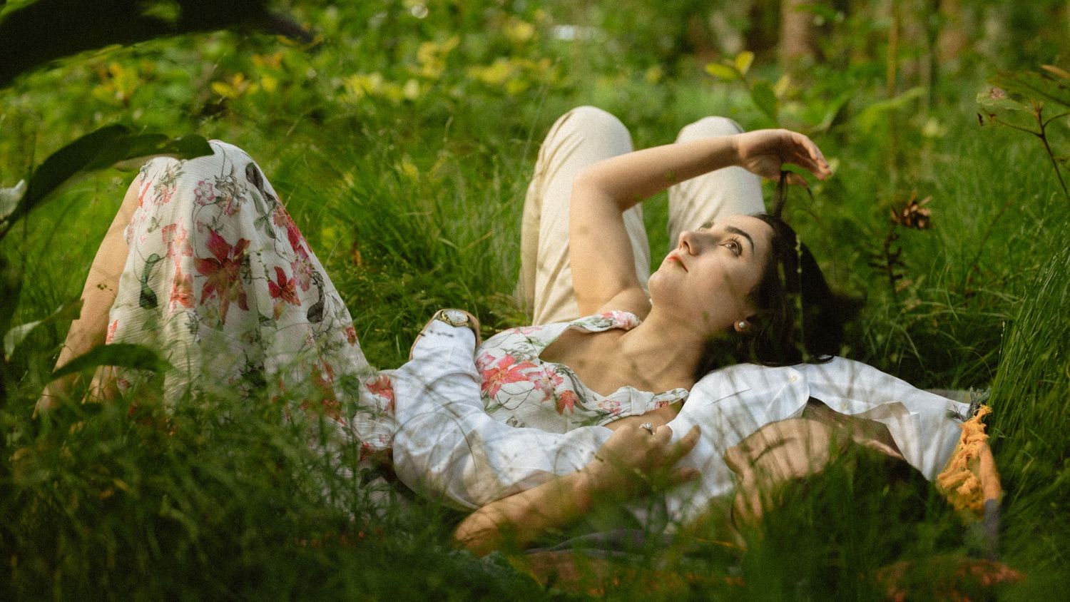 Person in floral dress lying on grass in artistic panoramic photo series.