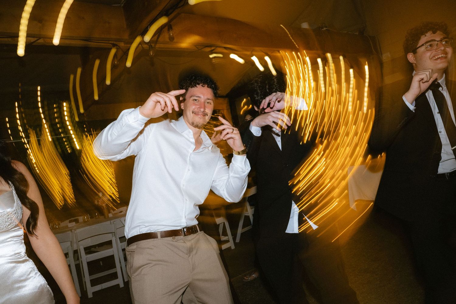 Two guests dancing joyfully at a wedding reception with swirling golden bokeh lights in the background.